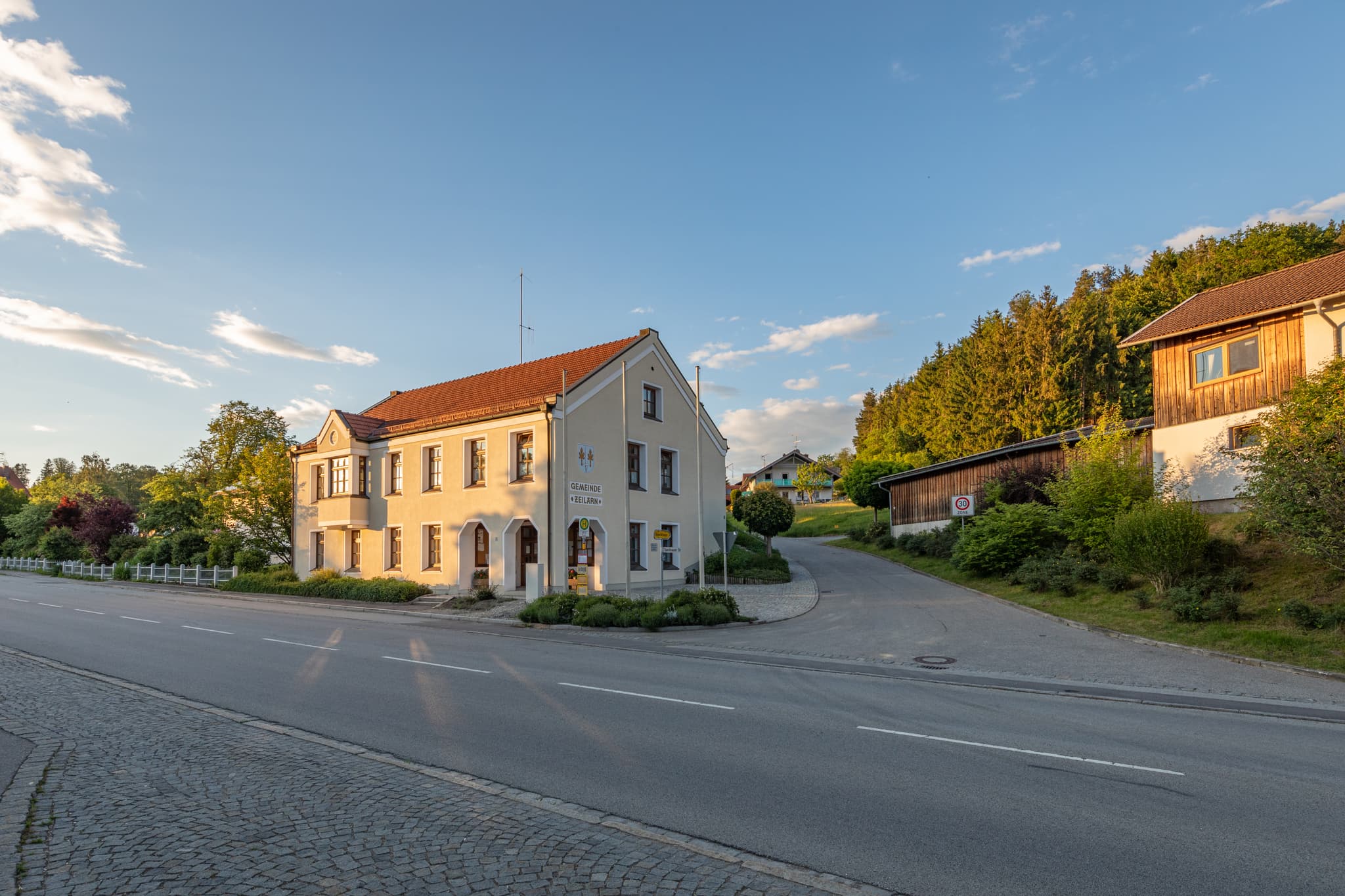 Das Gemeindehaus Gumpersdorf, Zeilarn, Rottal-Inn, Niederbayern. Ländliche Architektur im Bäderdrieck, Deutschland. Haus an Straße, Hügel und blauer Himmel.