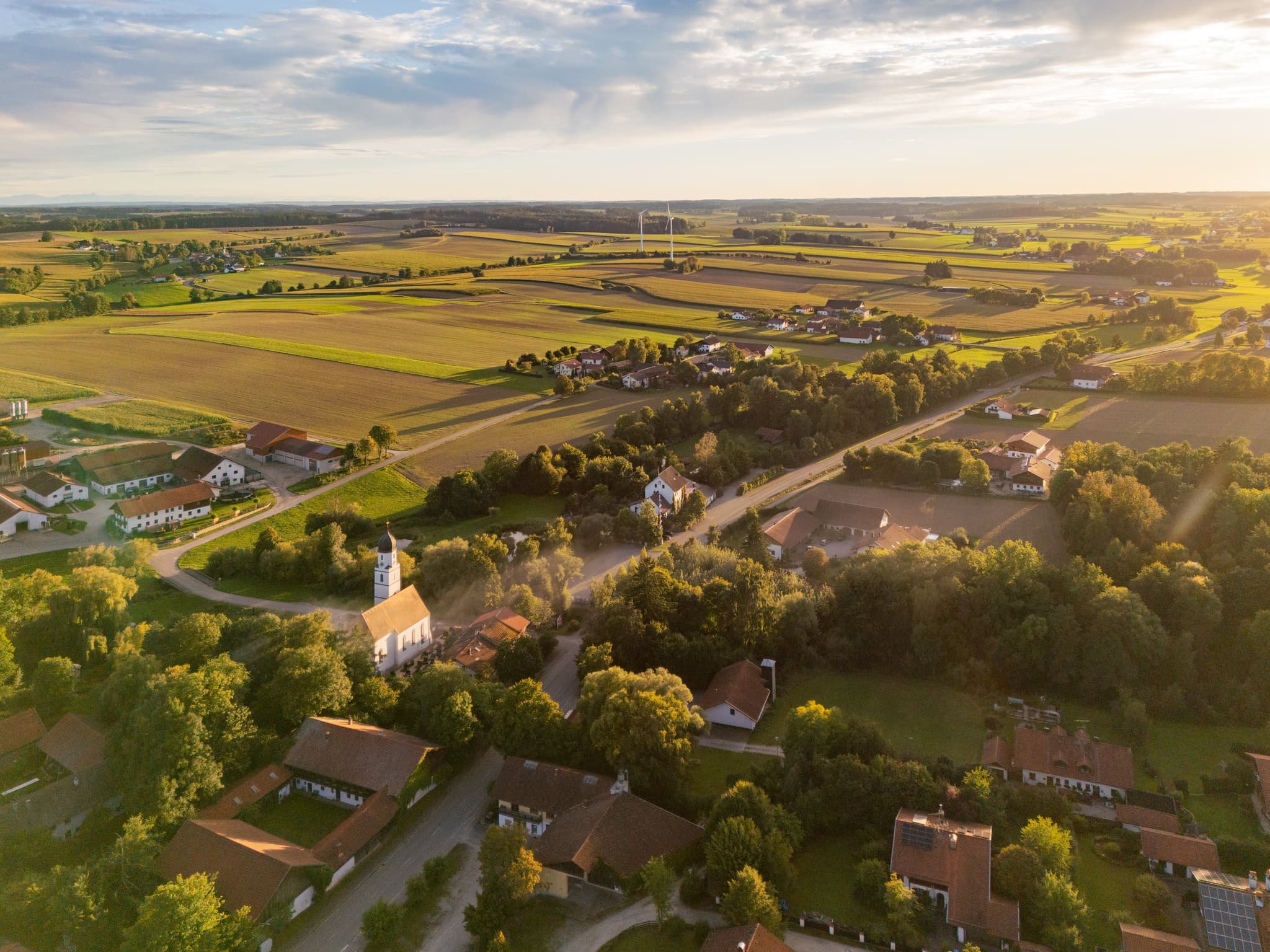 Ortsansicht Dirnaich, Gangkofen, Rottal-Inn, Niederbayern. Ein Windpark prägt die Landschaft im Holzland. Weite Felder unter Sonnenuntergang in Deutschland.