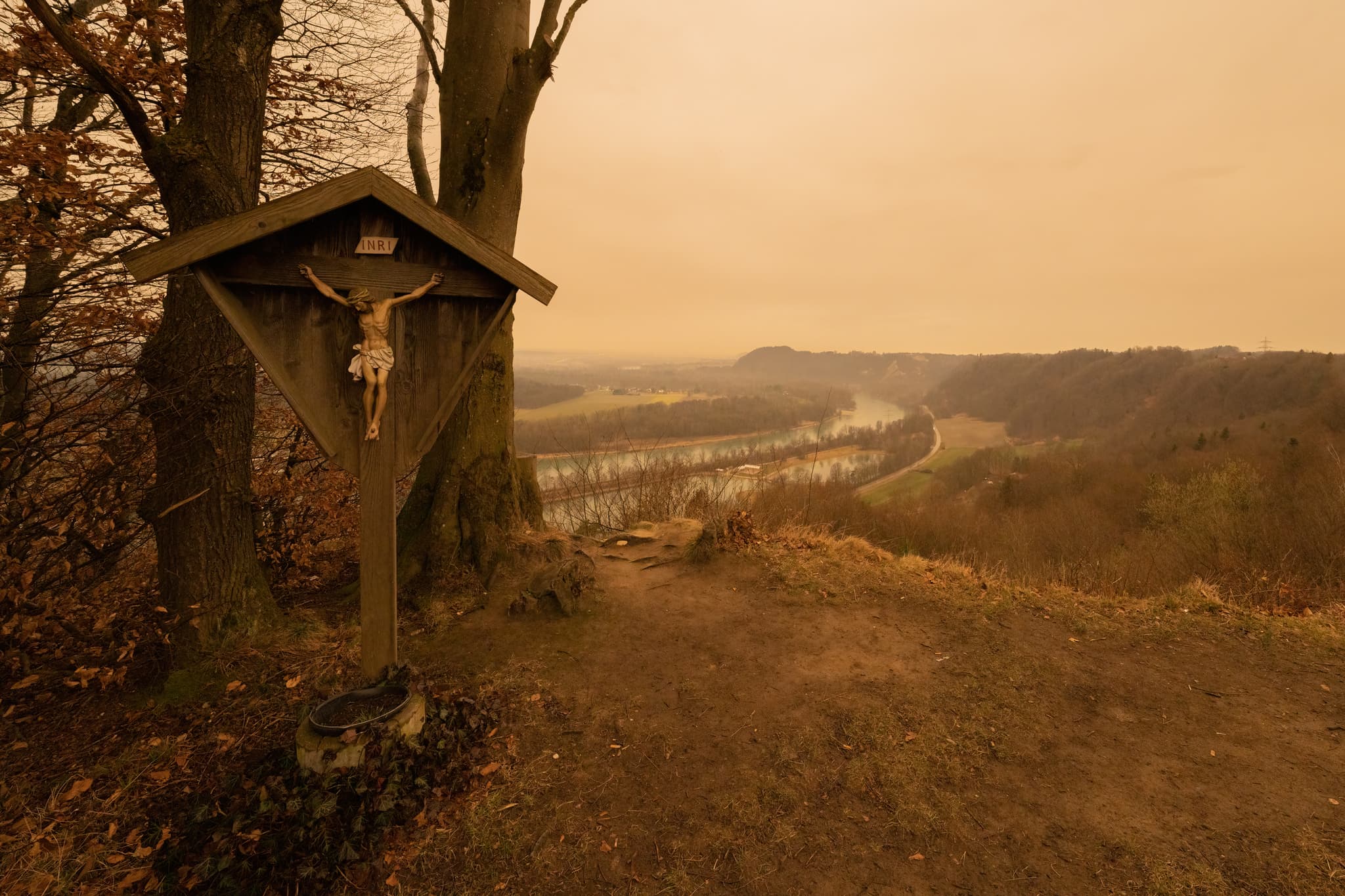 Aussicht bei Marktl, Landkreis Altötting, Region Inn-Salzach, Deutschland. Saharastaub trübt die Sicht auf die Landschaft. Ein Wegekreuz steht im Vordergrund.