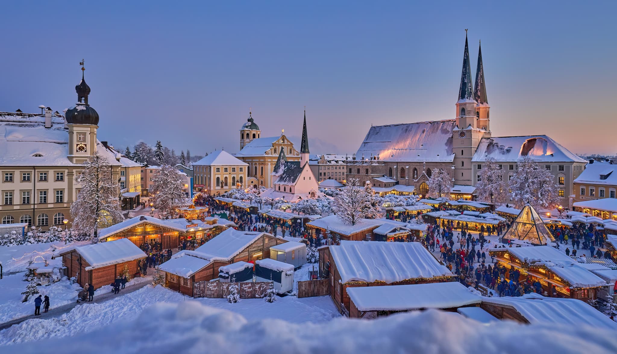 Erleben Sie den malerischen Weihnachtsmarkt in Altötting im winterlichen Glanz. Festliche Buden und schneebedeckte Dächer schaffen eine zauberhafte Atmosphäre.