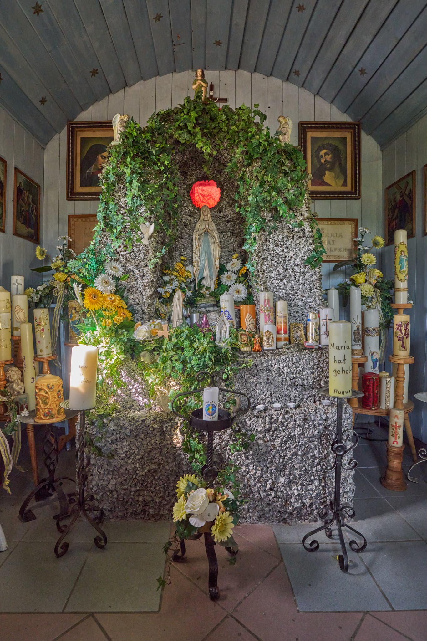 Innenansicht der Kapelle Stadlreith bei Tettenweis im Landkreis Passau, Niederbayern, Donau-Wald, Deutschland, zeigt Kerzen, Marienstatue und bunte Fenster.