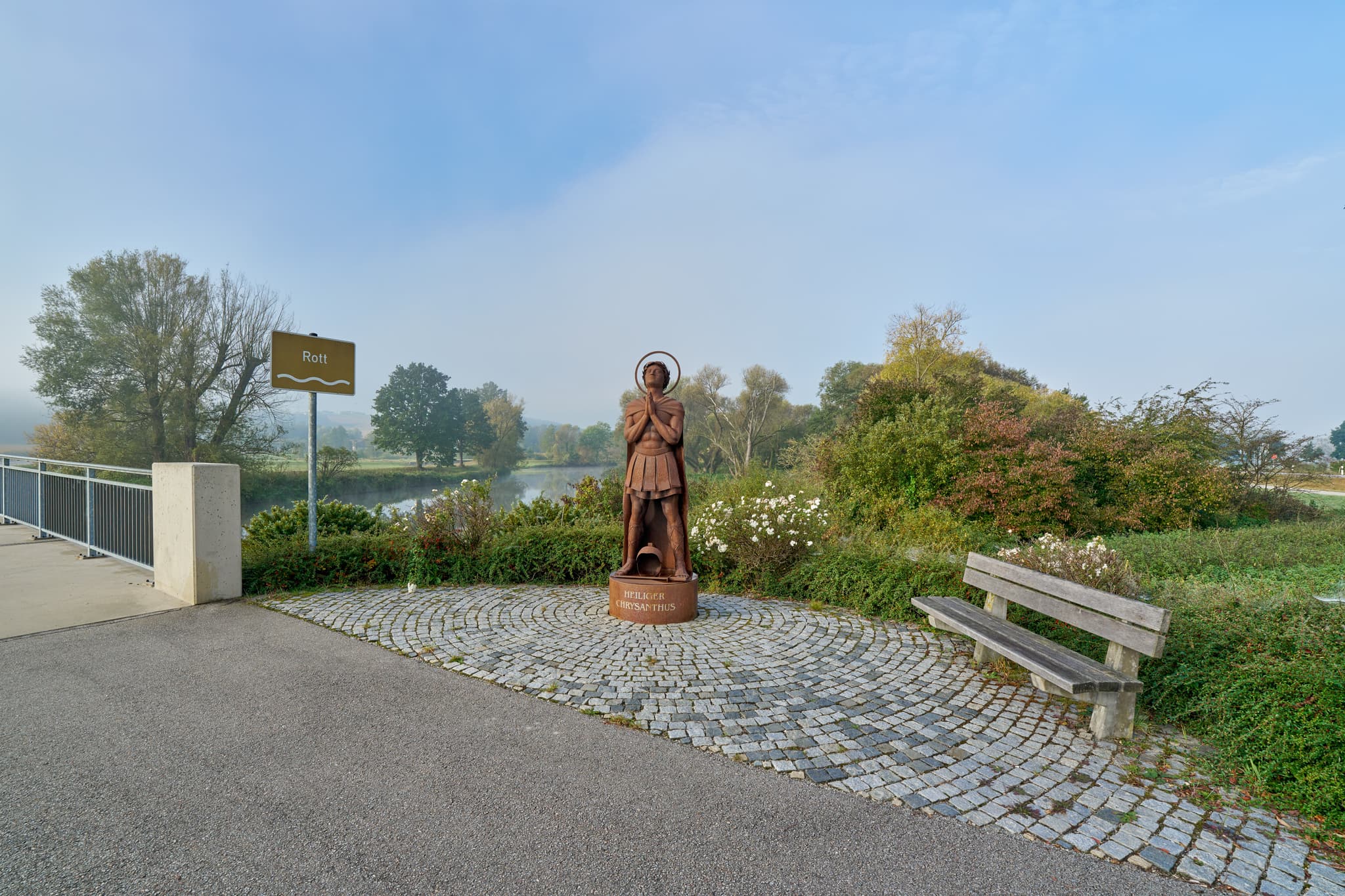 Die herbstliche Rottlandschaft in Bad Birnbach, Landkreis Rottal-Inn, Niederbayern, Region Bäderdreieck, Deutschland. Eine Statue mit Brücke und Fluss im Nebel.