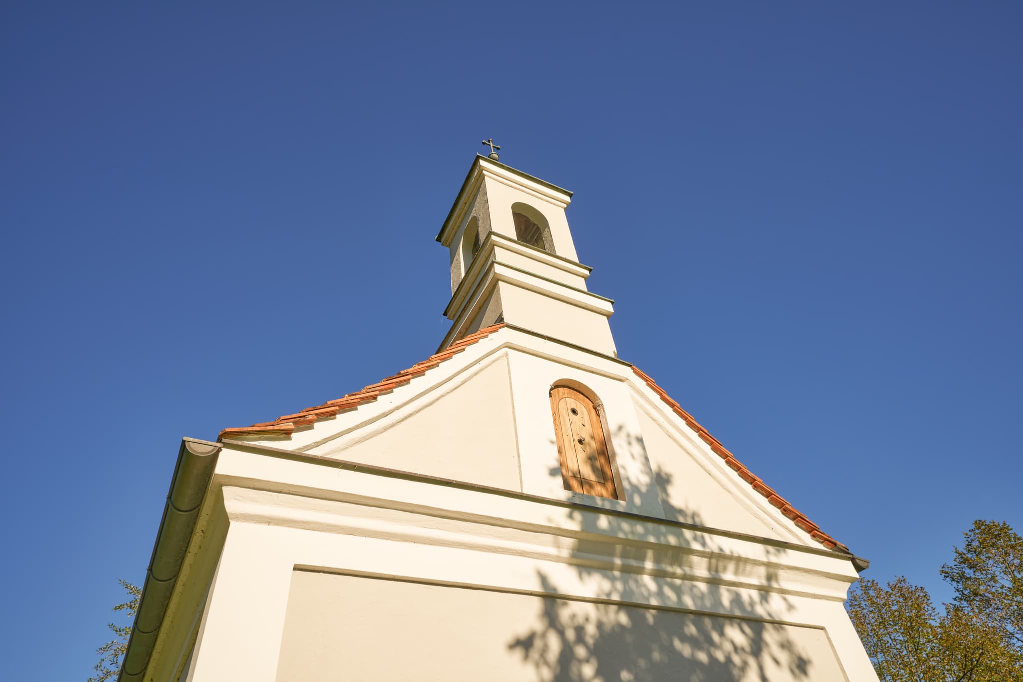 Kapelle in Ecksberg Altmühldorf Kronwidl, Mühldorf am Inn, Oberbayern, Inn-Salzach, Deutschland. Darstellung des Bauwerks mit Baumschatten unter blauem Himmel.