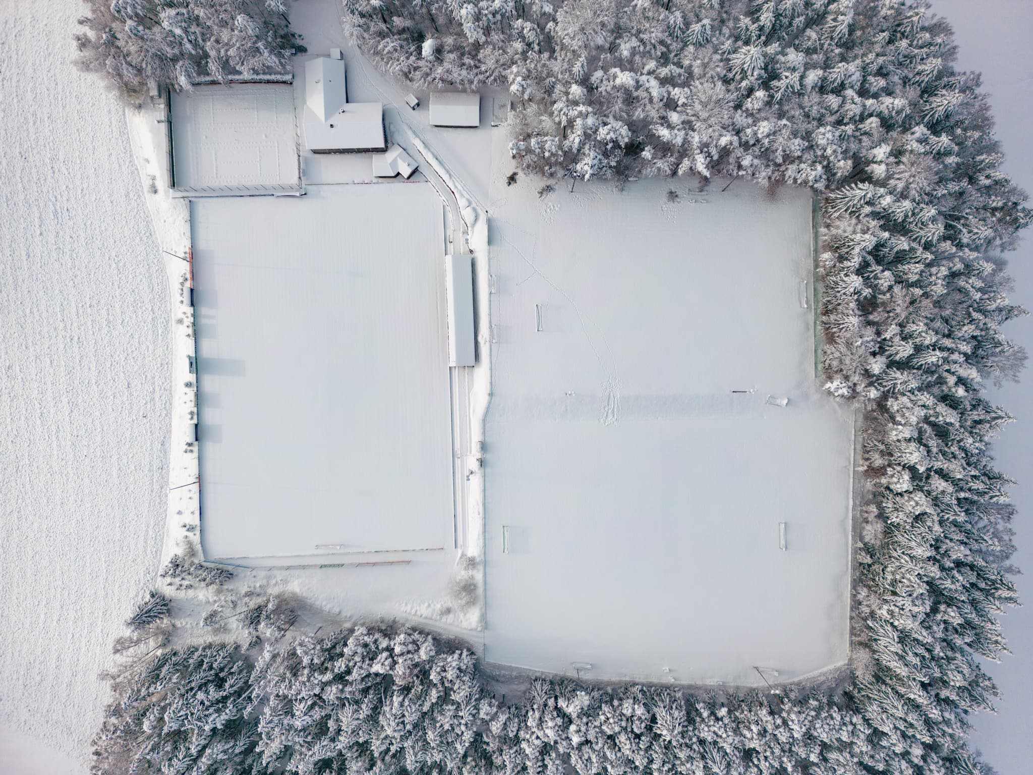 Winterliches Luftbild des Sportplatzes in Erlbach, Landkreis Altötting, Oberbayern. Die schneebedeckten Felder sind umgeben von verschneiten Bäumen. Inn-Salzach
