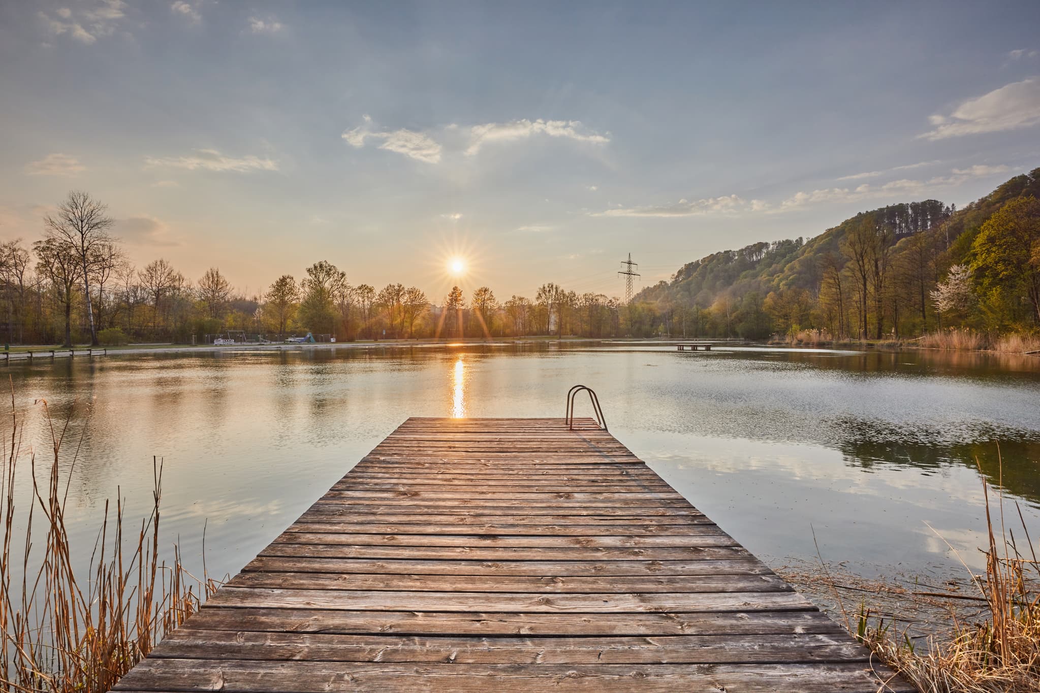 Genießen Sie den Sonnenuntergang am Marktler Badesee in Oberbayern, Inn-Salzach Region, Deutschland. Ein idyllischer Holzsteg lädt zum Verweilen ein.