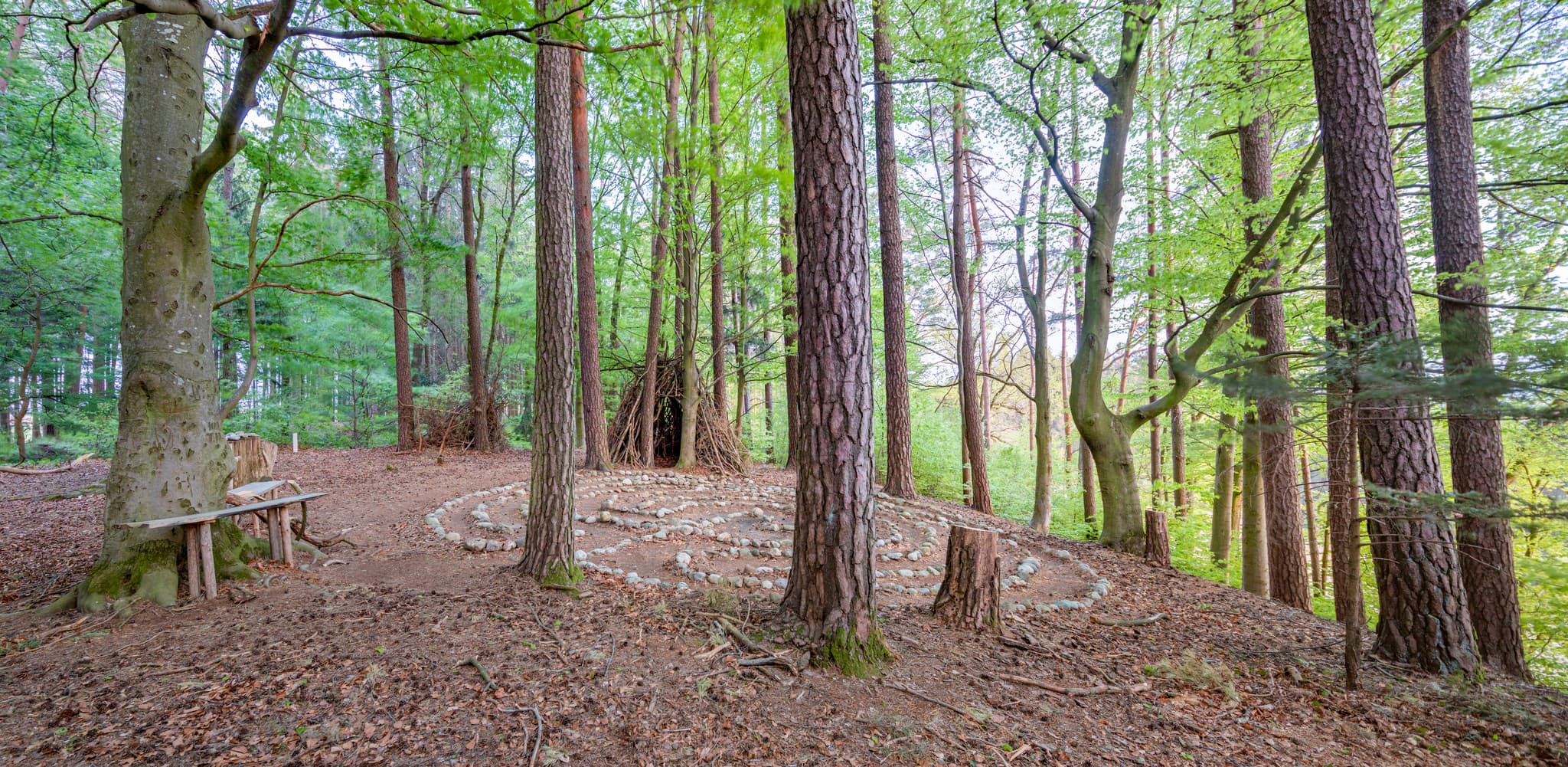 Ein Steinlabyrith in einem Wald bei Zeilarn, Rottal-Inn, Niederbayern, Deutschland. Das Holzland prägt die Landschaft mit Bäumen. Holzbank und Ast-Tipi.