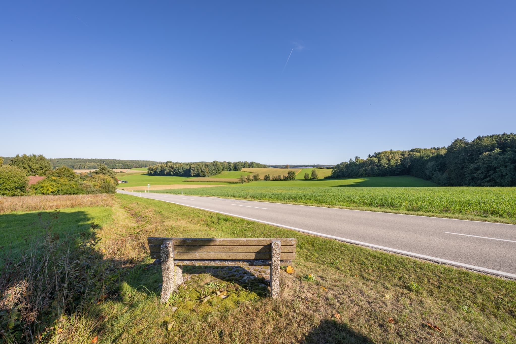 Bank am Straßenrand in Baumgarten, Dietersburg. Ländliche Landschaft im Landkreis Rottal-Inn, Niederbayern, Deutschland, zeigt Felder und Wälder im Holzland.