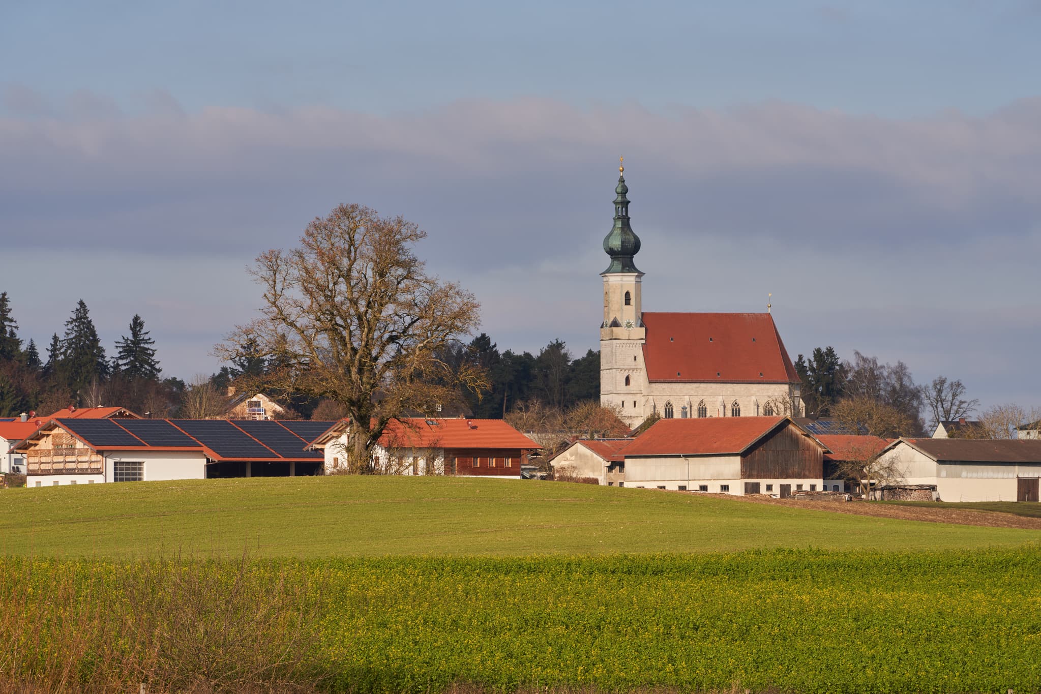 Dorfansicht von Asten bei Tittmoning in Oberbayern, Region Inn-Salzach, Deutschland. Die Kirche im Hintergrund prägt das Bild. Sonnige Landschaft mit Feldern.