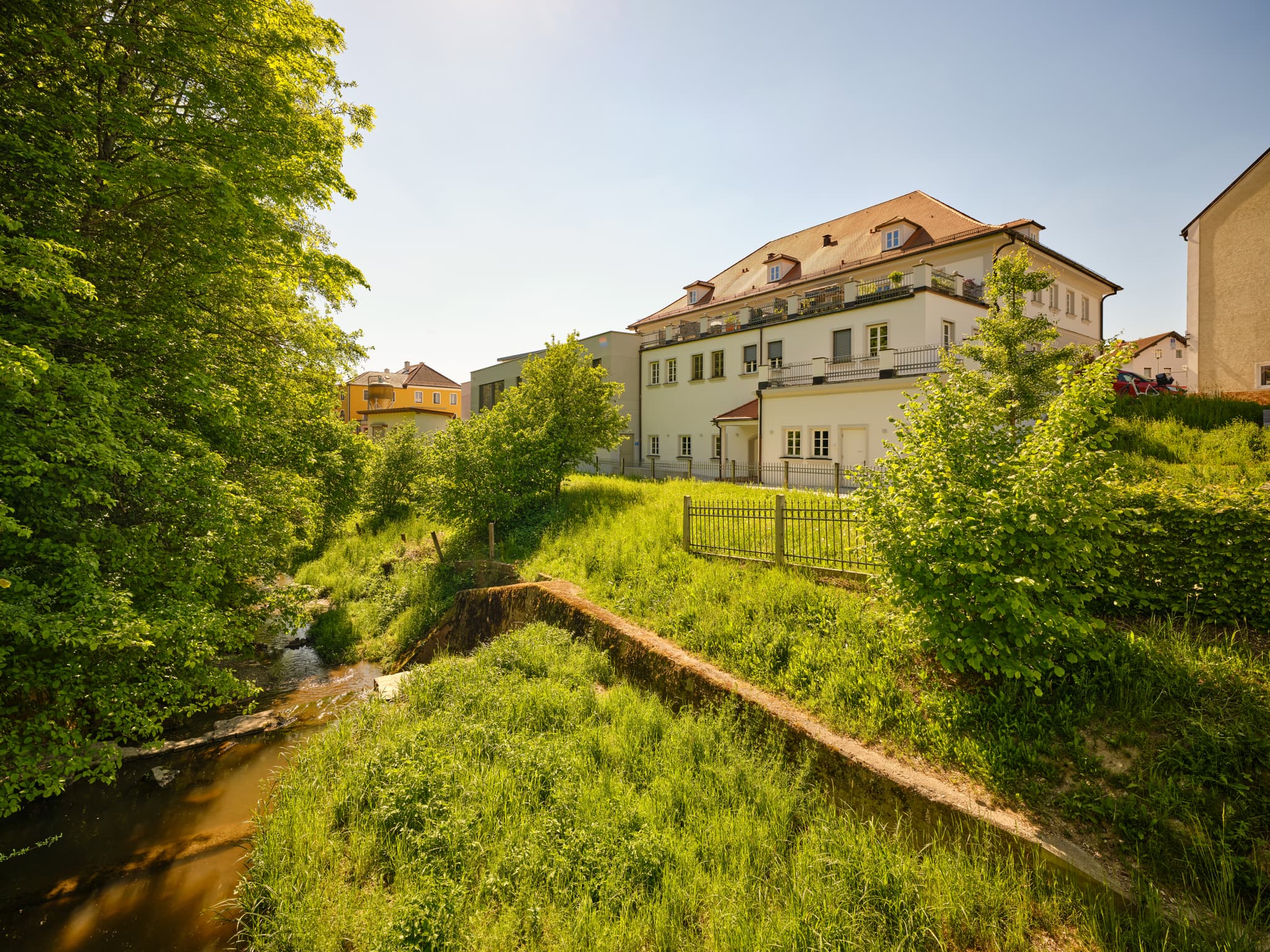 Ansicht Reischach, Altötting, Oberbayern, Deutschland. Bach und grüne Ufer. Markantes Gebäude mit rotem Dach. Typisch für die malerische Inn-Salzach Region.