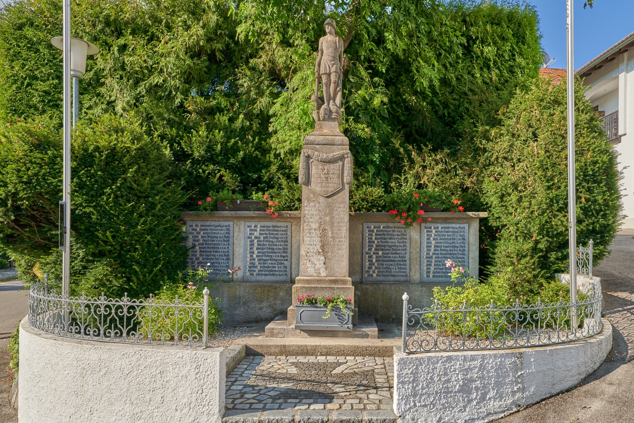 Das Kriegerdenkmal in Niedertaufkirchen, Mühldorf am Inn, Oberbayern, ist ein detailreiches Monument. Umgeben von Grün und Zaun, dient es als Gedenkort.