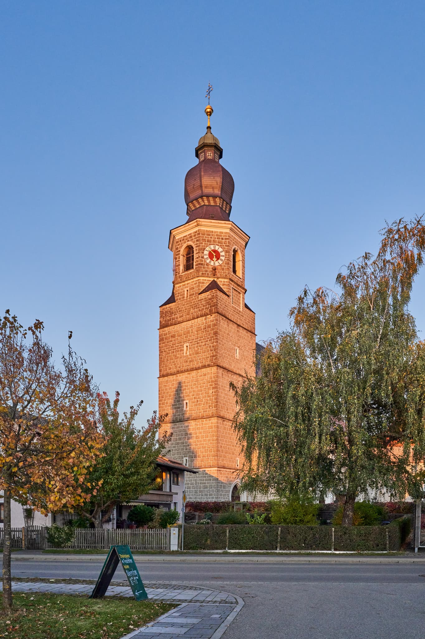 Kirche Mariä Himmelfahrt, Feichten, Altötting, Oberbayern, Deutschland. Ihr Kirchturm prägt Ortsbild der Inn-Salzach Region. Umgeben von Bäumen und Gebäuden.