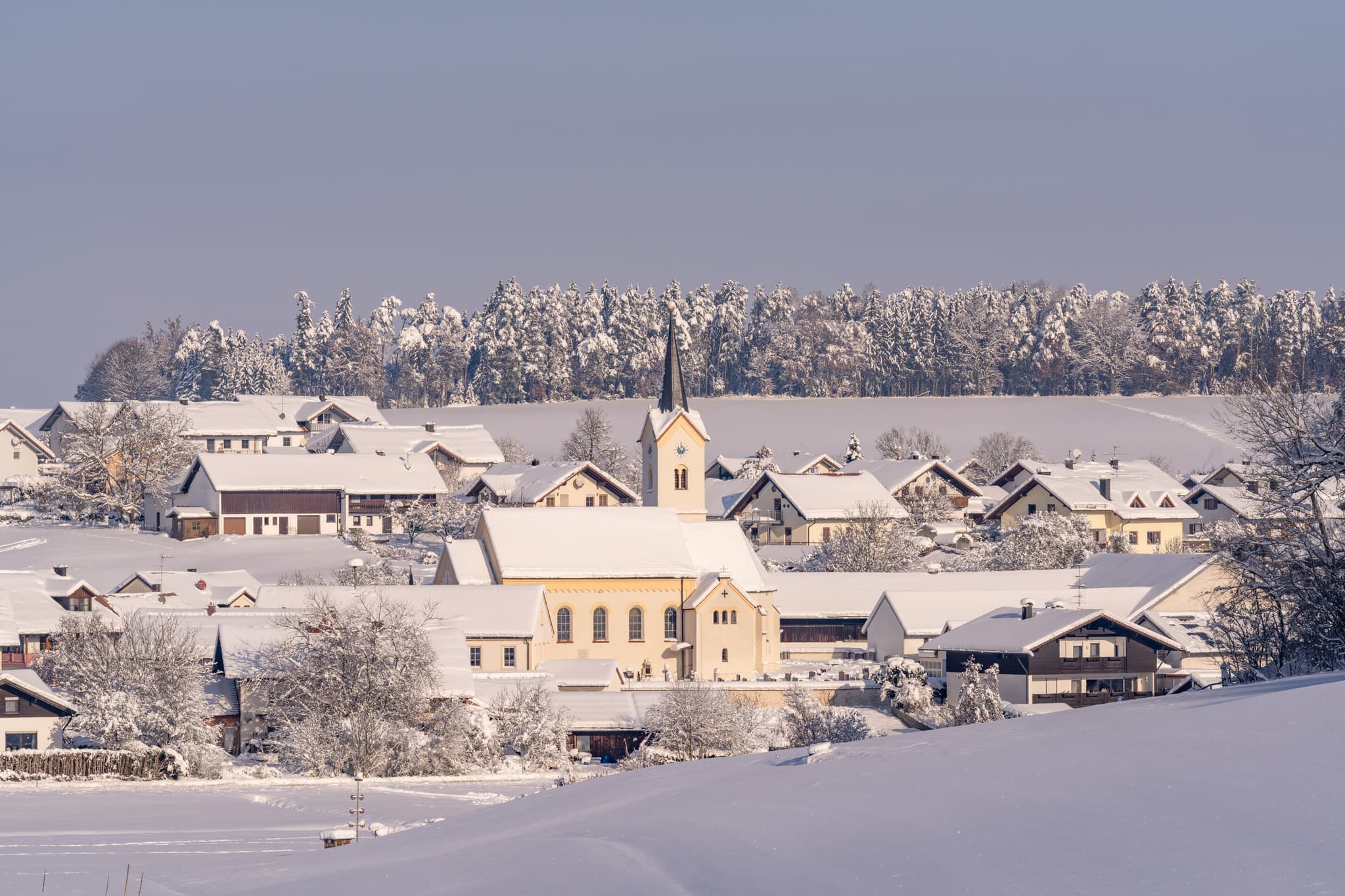 Winterliches Erlbach im Landkreis Altötting, Oberbayern, Deutschland. Das Bild zeigt das verschneite Dorf mit der zentralen Kirche in der Inn-Salzach Region.
