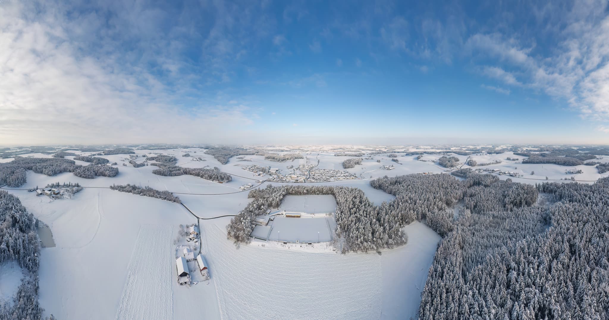 Luftbild Sportplatz Erlbach, Altötting, Oberbayern. Winterlandschaft Inn-Salzach Deutschland. Verschneite Felder, Wälder und Gebäude unter blauem Himmel.