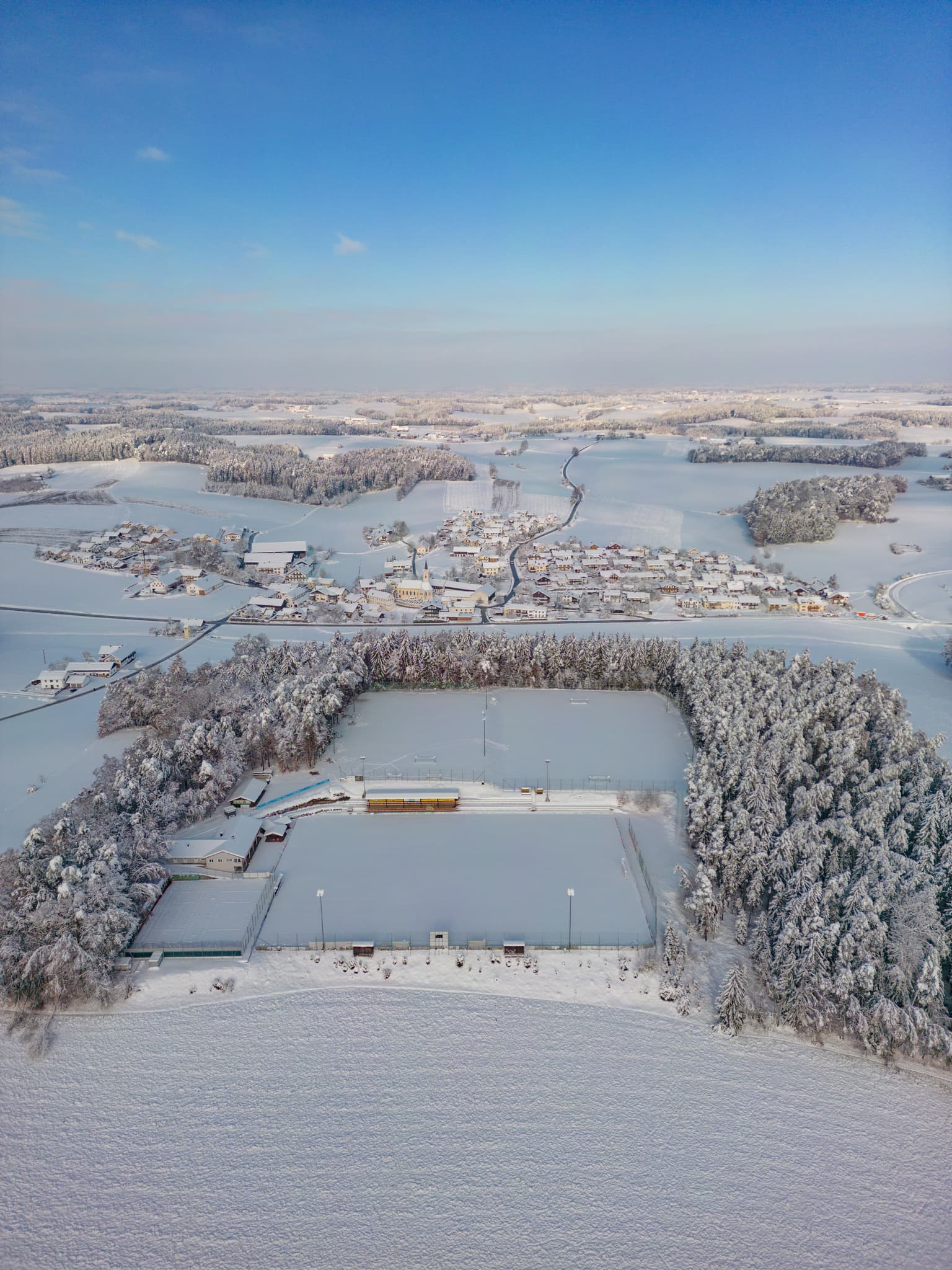 Luftbild des verschneiten Sportplatzes in Erlbach, Landkreis Altötting, Oberbayern, Deutschland. Prägnante Winterlandschaft in der Inn-Salzach Region.