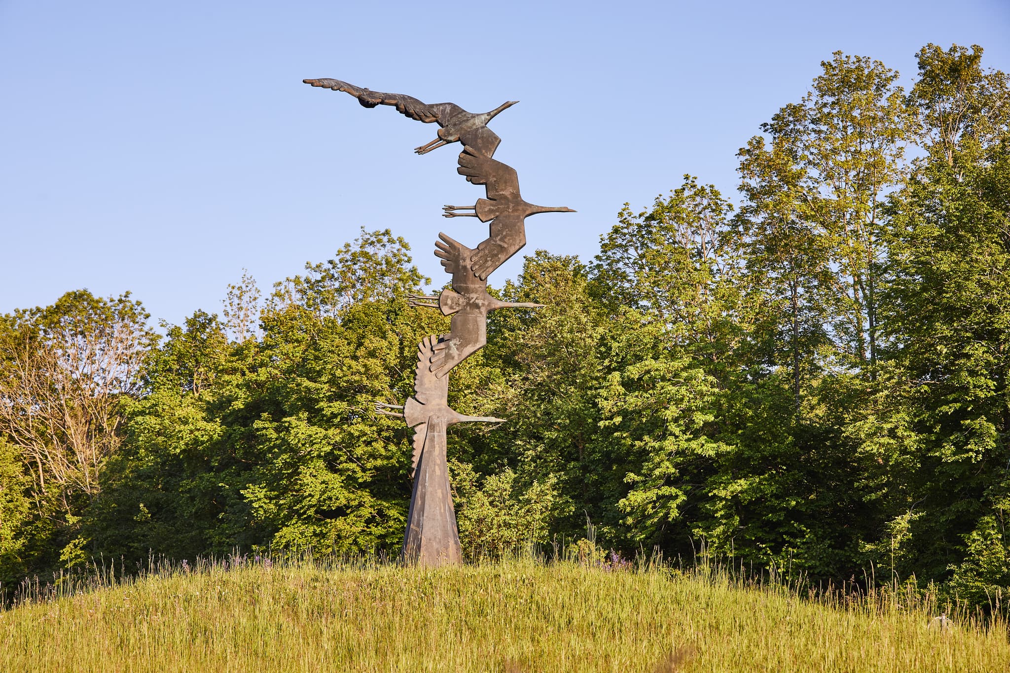 Kranich-Skulptur auf grasbewachsenem Hügel in Hohenwart, Emmerting, Altötting, Oberbayern. Fliegende Kraniche als Motiv in der Region Inn-Salzach, Deutschland.