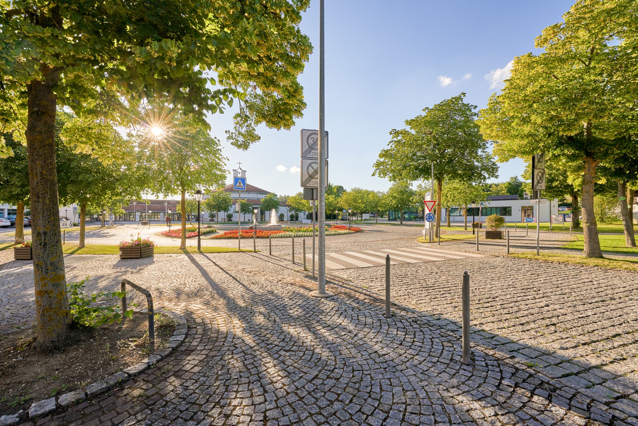 Sonniger Blick auf die Kurallee in Bad Griesbach, Passau, Niederbayern. Einladender Platz im Donau-Wald, Deutschland, mit Bäumen, Pflastersteinen und Brunnen.