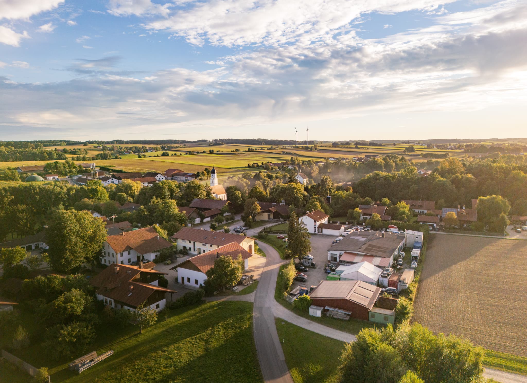 Ortsansicht Dirnaich, Gangkofen, Rottal-Inn, Niederbayern. Ein Windpark prägt die Landschaft im Holzland. Weite Felder unter Sonnenuntergang in Deutschland.