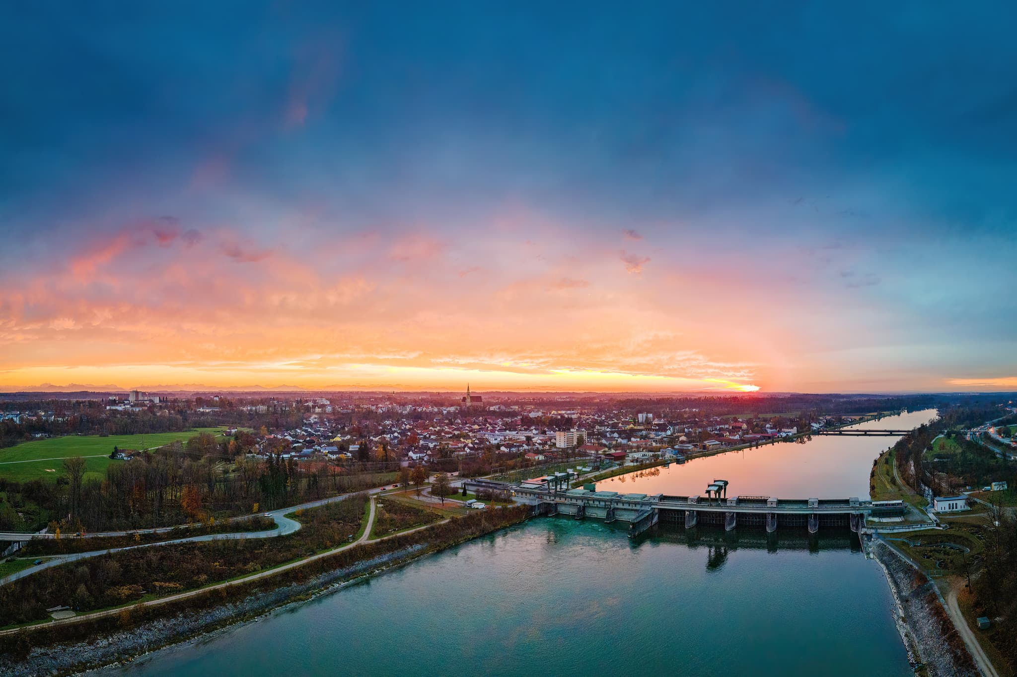 Sonnenuntergang über Neuötting, Landkreis Altötting, Oberbayern. Panorama des Inns mit Wehr und Stadtansicht bei Dämmerung.