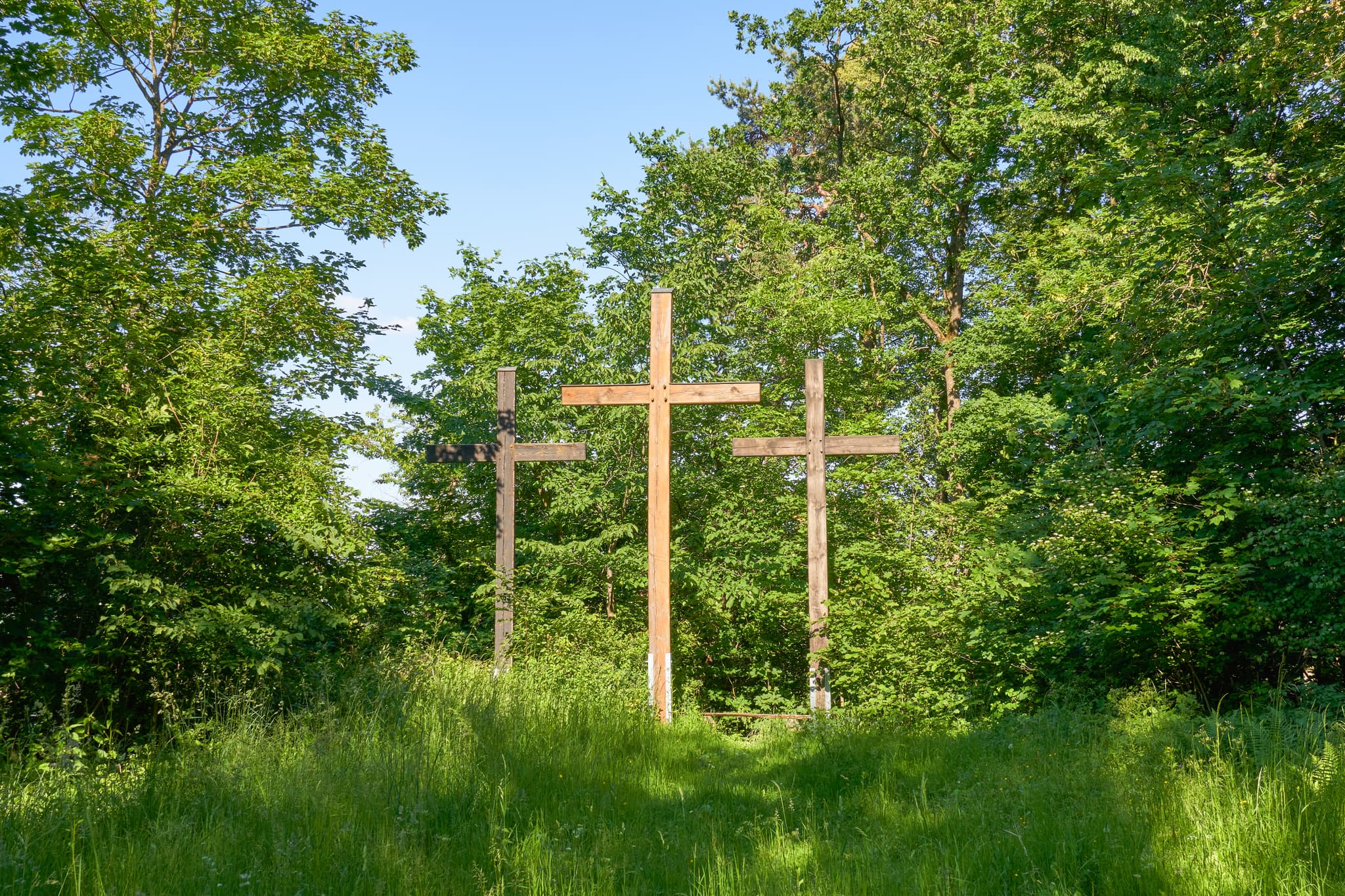 Drei Holzkreuze auf dem Kalvarienberg in Neuötting, Altötting, Oberbayern. Eingebettet in grüne Wiesen und hohe Bäume, typisch für die Region Inn-Salzach.