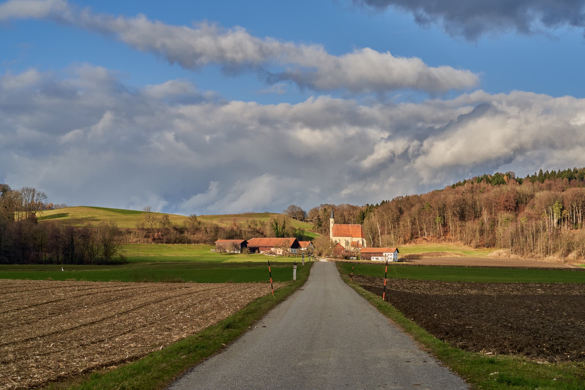 Wallfahrtskirche St. Anna, Ering, Rottal-Inn, Niederbayern, Holzland, Deutschland. Weg durch Felder, umgeben von Hügeln und Wald unter bewölktem Himmel.