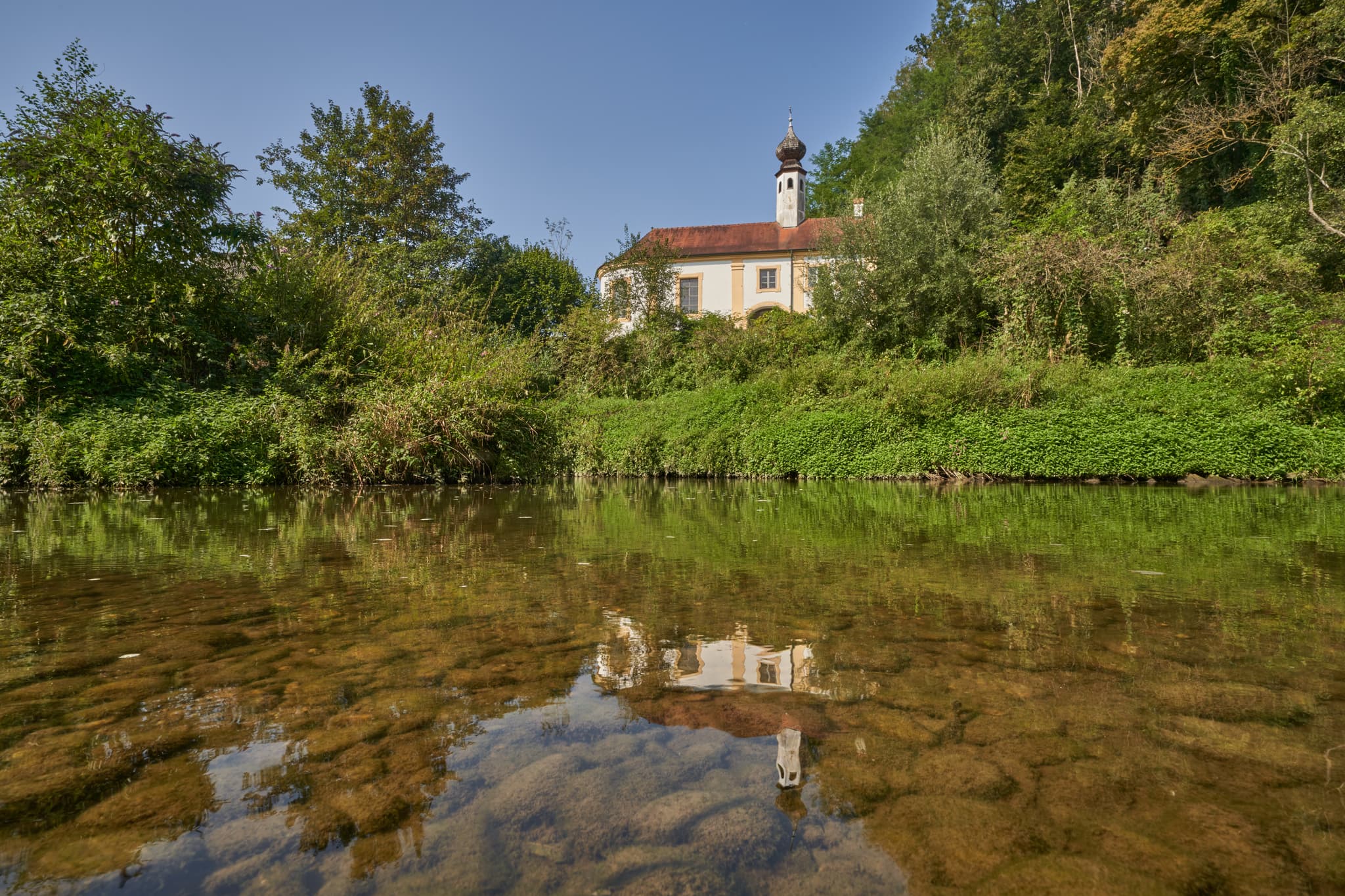 Die malerische Klausenkirche Engfurt in Töging am Inn, Landkreis Altötting, Oberbayern, Region Inn-Salzach, Deutschland, spiegelt sich im Wasser.