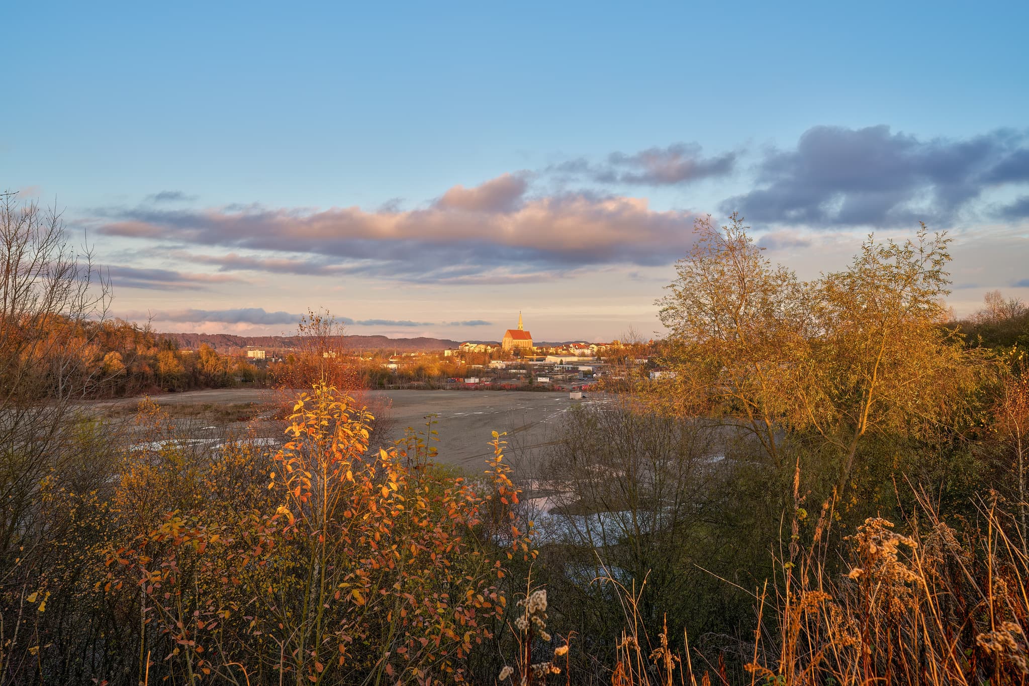 Blick von der Kiesgrube Neuötting, Landkreis Altötting, Oberbayern, Deutschland auf die Stadtpfarrkirche St. Nikolaus. Inn-Salzach im goldenen Abendlicht.