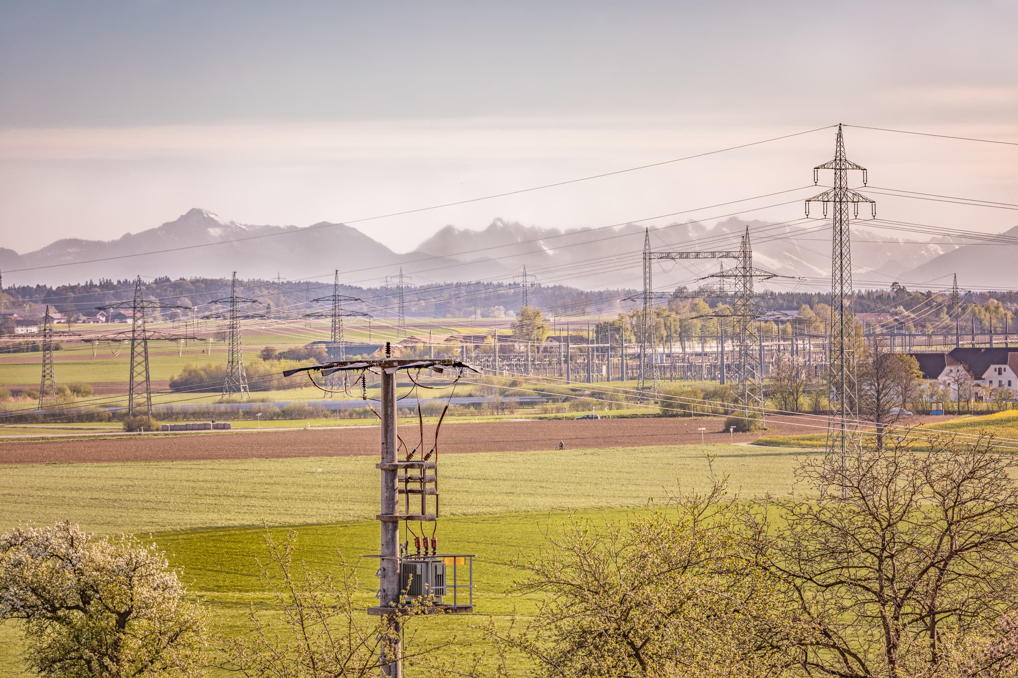 Landschaftsbild der Eschlberg Aussicht in Mehring, Altötting, Oberbayern, Deutschland. Zeigt Felder, Strommasten, Umspannwerk und die Alpen im Hintergrund.