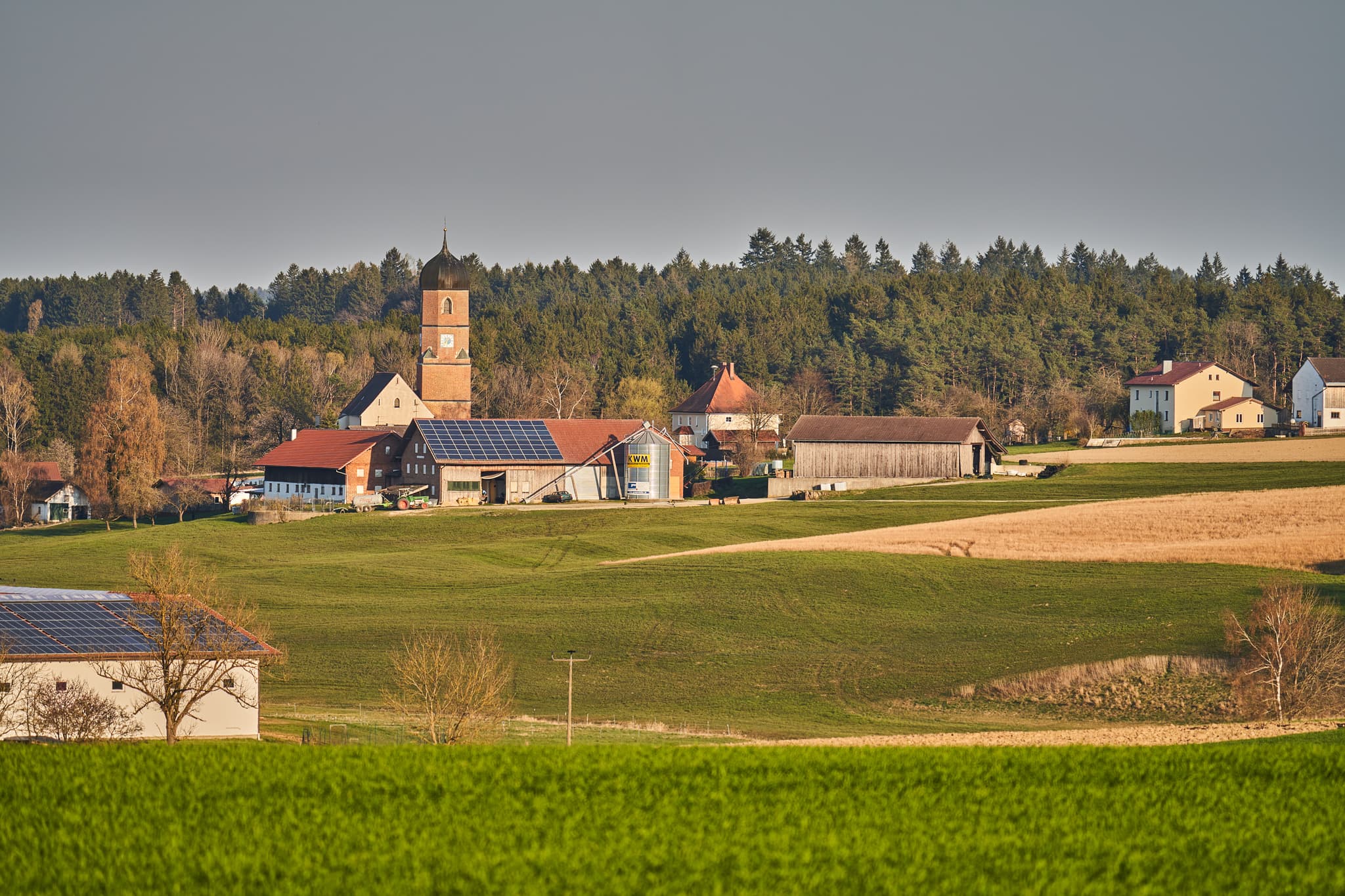 Kirche und Bauernhöfe mit Solaranlagen in Martinskirchen, Wurmannsquick, Landkreis Rottal-Inn, Niederbayern. Typische Landschaft des Holzlands, Deutschland.