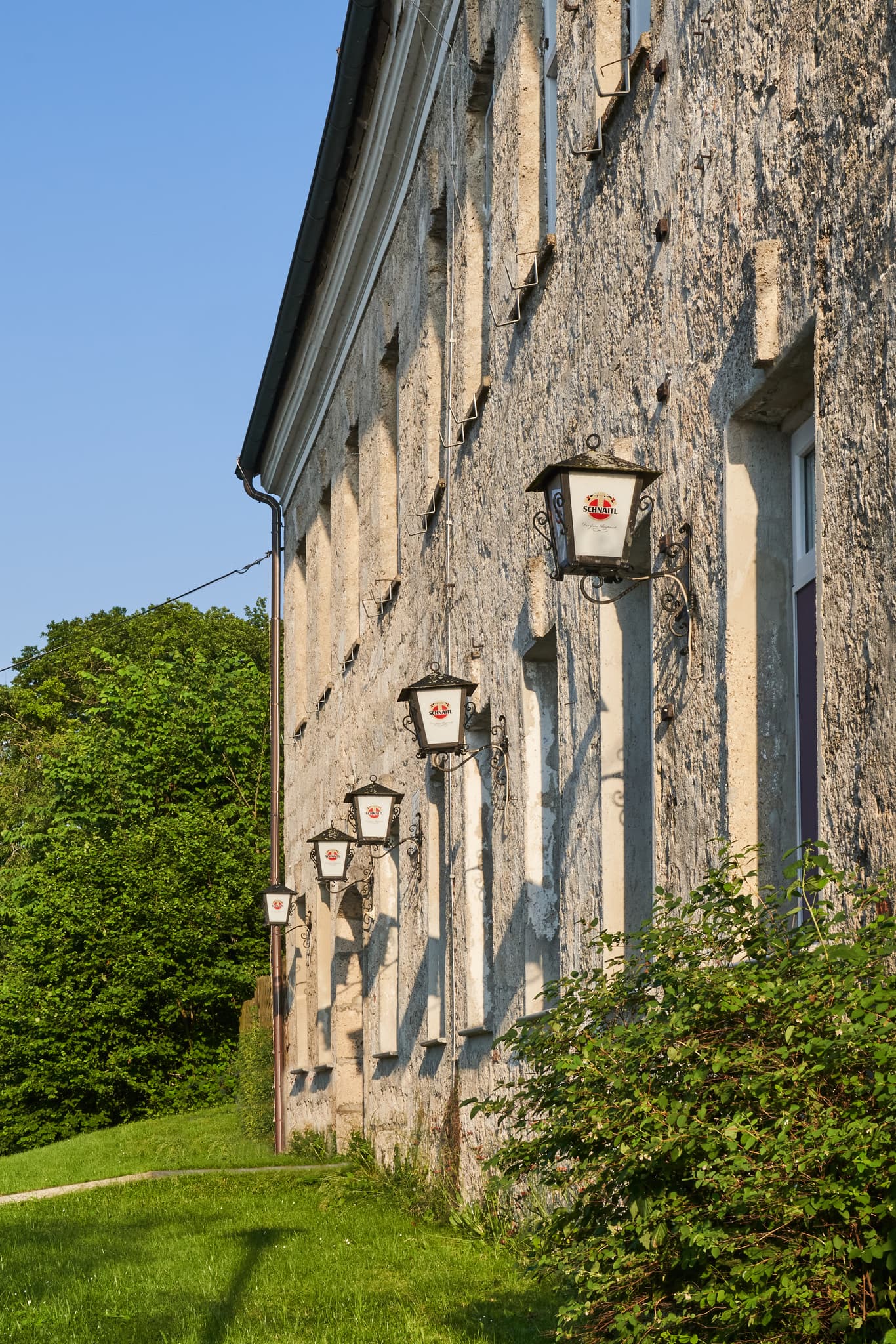 Historische Frauenstein Burg in Mining, Braunau am Inn, Oberösterreich. Alte Steinmauer mit Laternen im Innviertel, Österreich, und grüner Landschaft.