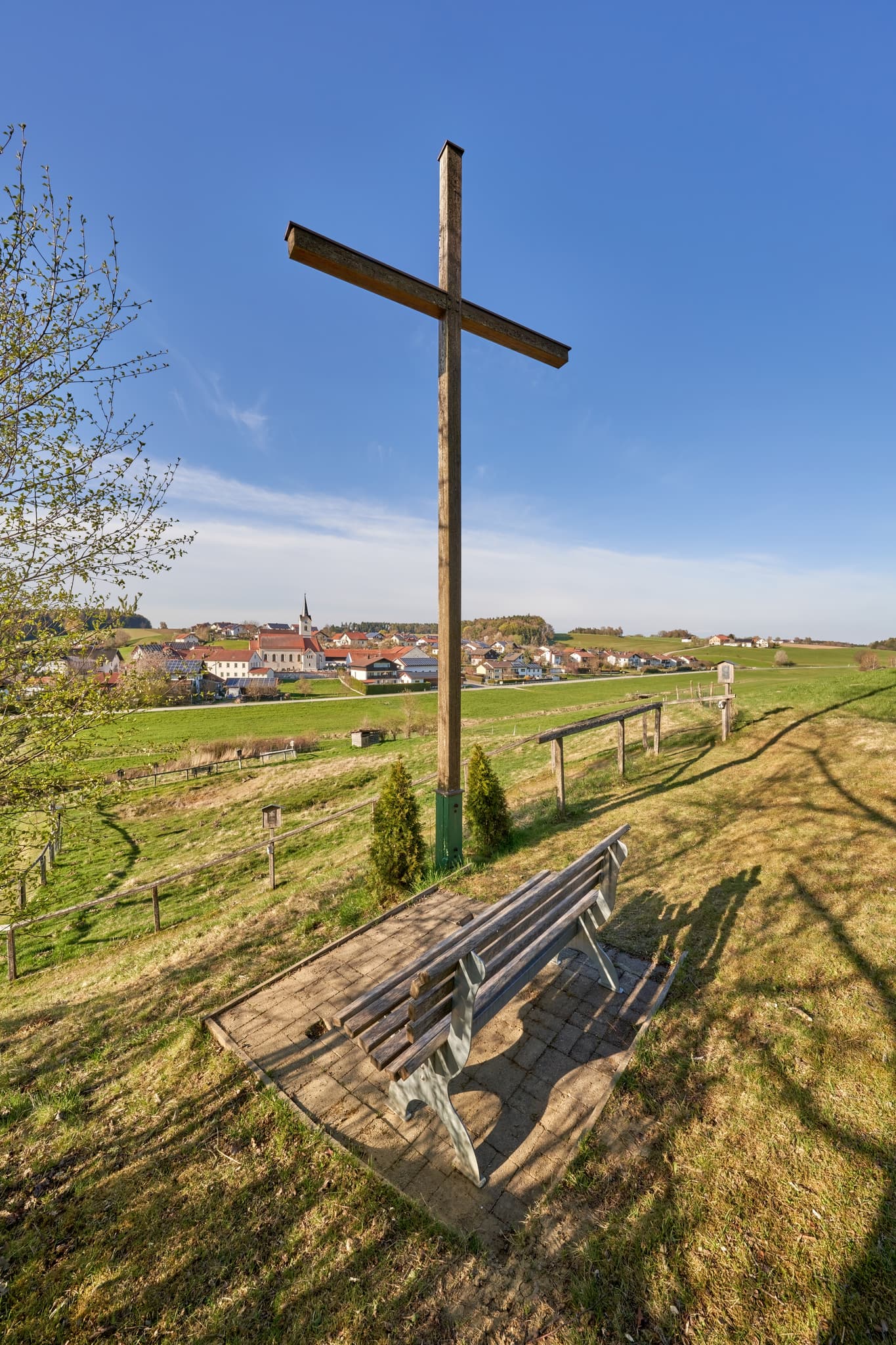 Holzkreuz mit Bank am Kreuzweg in Erlbach, Altötting, Oberbayern. Das Bild zeigt einen Ausblick über die Hügellandschaft, Oberbayern, Deutschland.