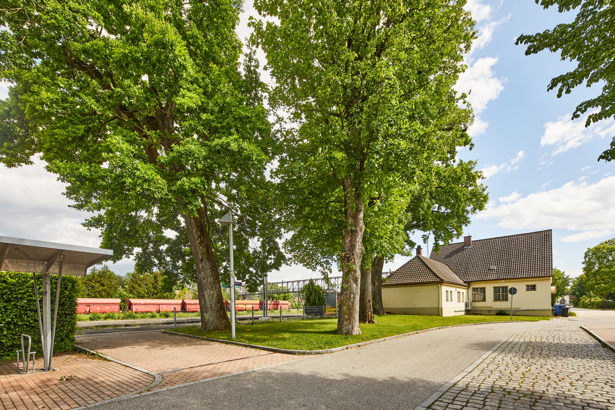 Bahnhof in Garching a.d. Alz, Landkreis Altötting, Oberbayern, Region Inn-Salzach, Deutschland. Vorplatz mit alten Bäumen.