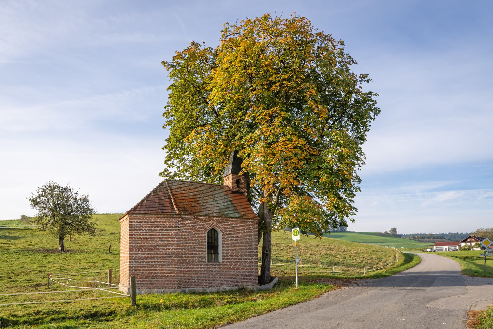 Idyllische Kapelle in Steina, Bad Birnbach, Rottal-Inn, Niederbayern. Das kleine Backsteingebäude mit hohem Baum prägt die Landschaft umgeben von Feldern.