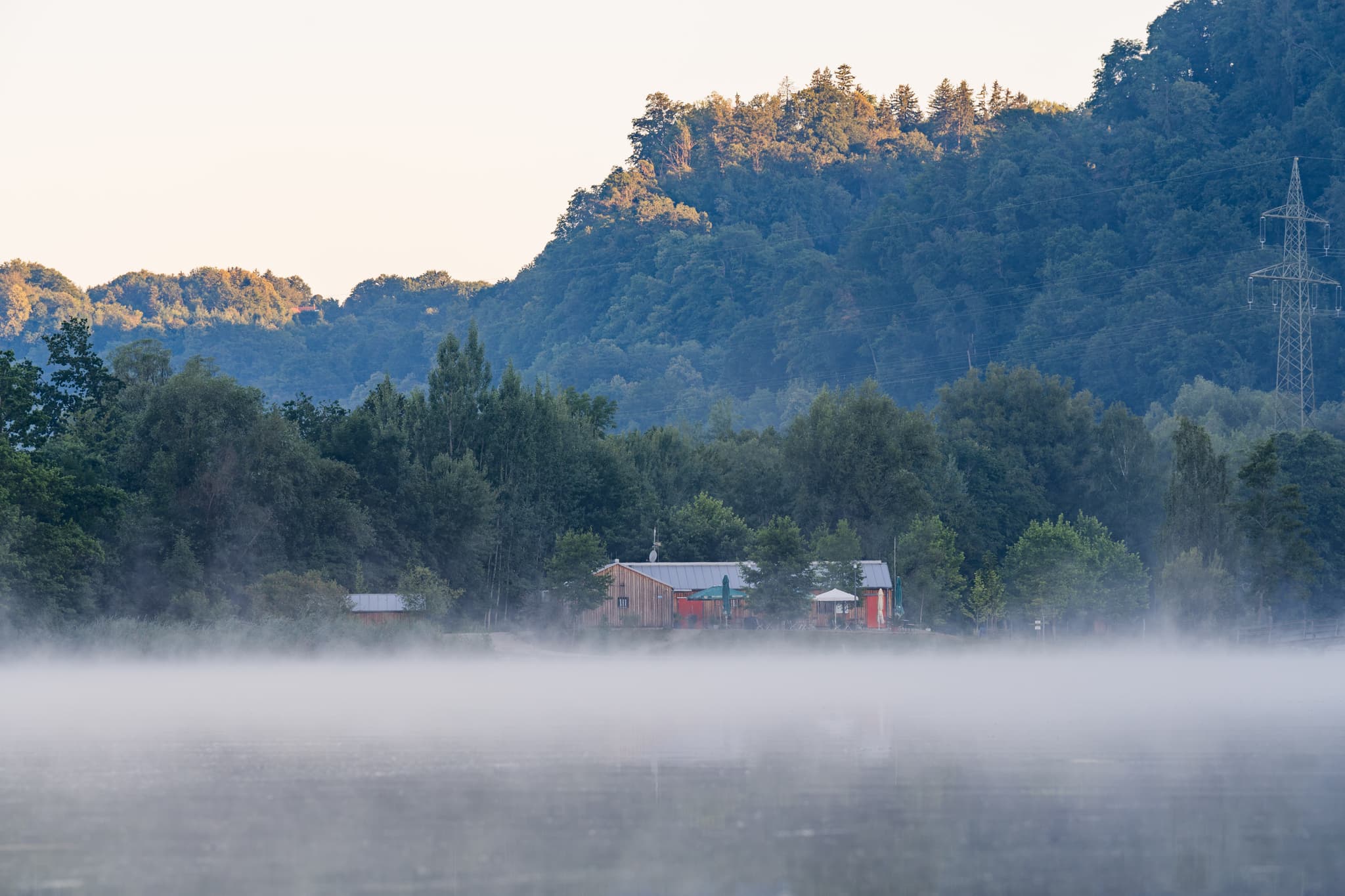 Badesee in Marktl, Altötting, Oberbayern, Deutschland: Morgennebel über dem See. Klare Sicht auf die Landschaft der Region Inn-Salzach.