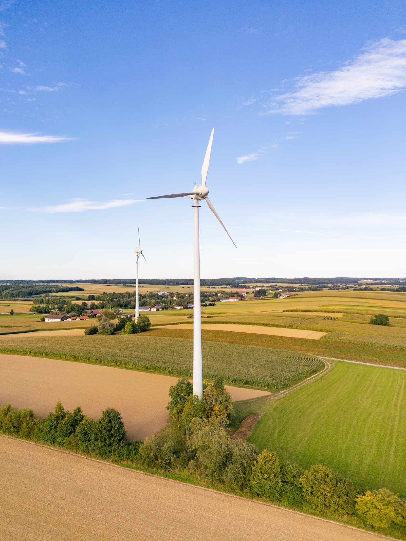 Zwei Windkraftanlagen inmitten weitläufiger Felder und grüner Landschaft bei Dirnaich, Gangkofen, im Landkreis Rottal-Inn, Niederbayern, Holzland.