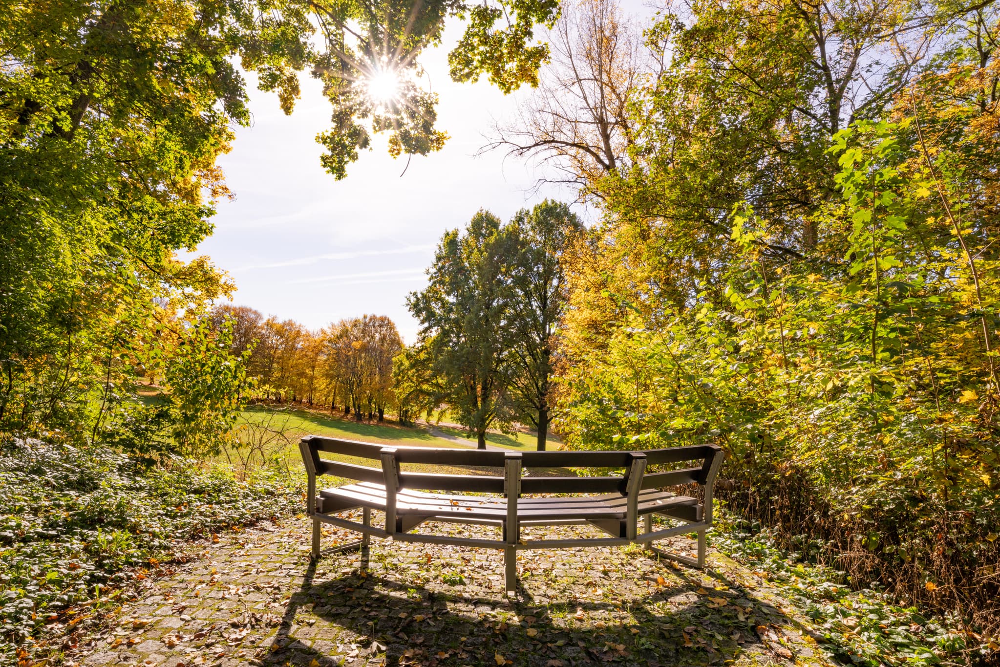 Herbstliche Impressionen aus dem Kurpark der Therme Bad Griesbach, Passau, Niederbayern. Eine einladende Bank inmitten der bunten Natur im Rottal, Deutschland.