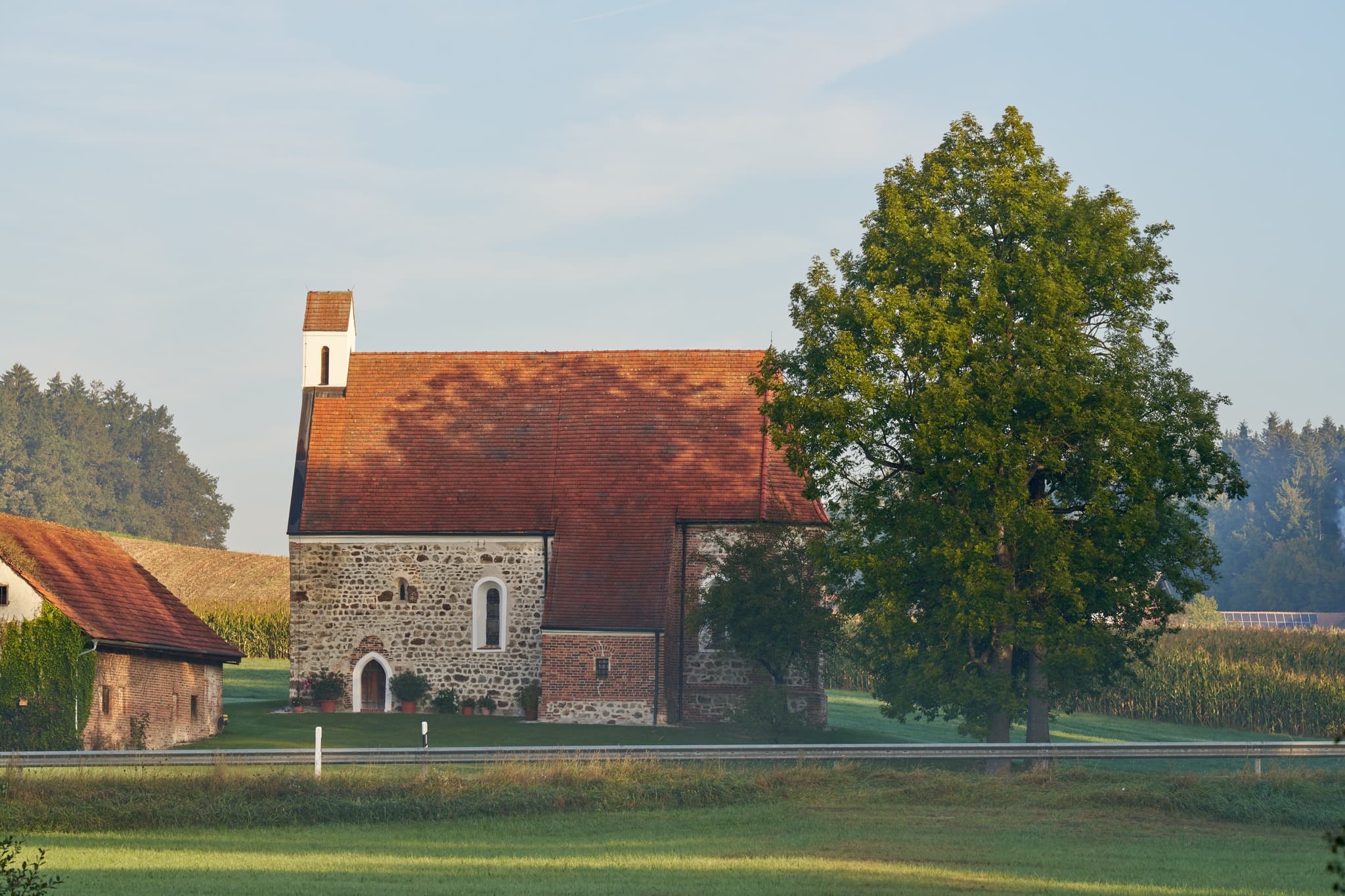 Filialkirche in Schreihof, Postmünster, Landkreis Rottal-Inn, Niederbayern, Deutschland. Ländliche Umgebung im Holzland mit Kirche, Baum und Feldern.
