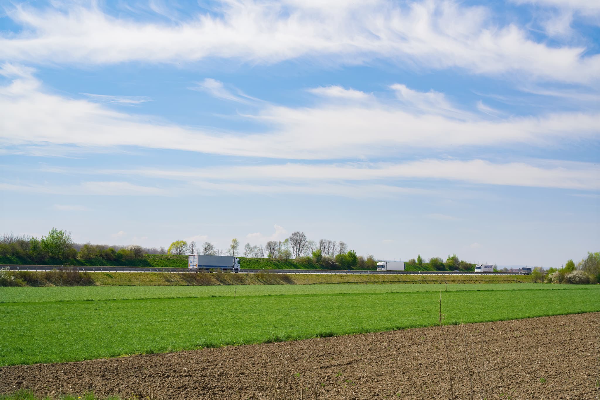 Landschaft um Stegmühle mit A94, Mühldorf am Inn. Grüne Felder, Acker. Autobahn A94 mit LKWs. Landkreis Mühldorf am Inn, Oberbayern. Weiter Himmel, Bäume.
