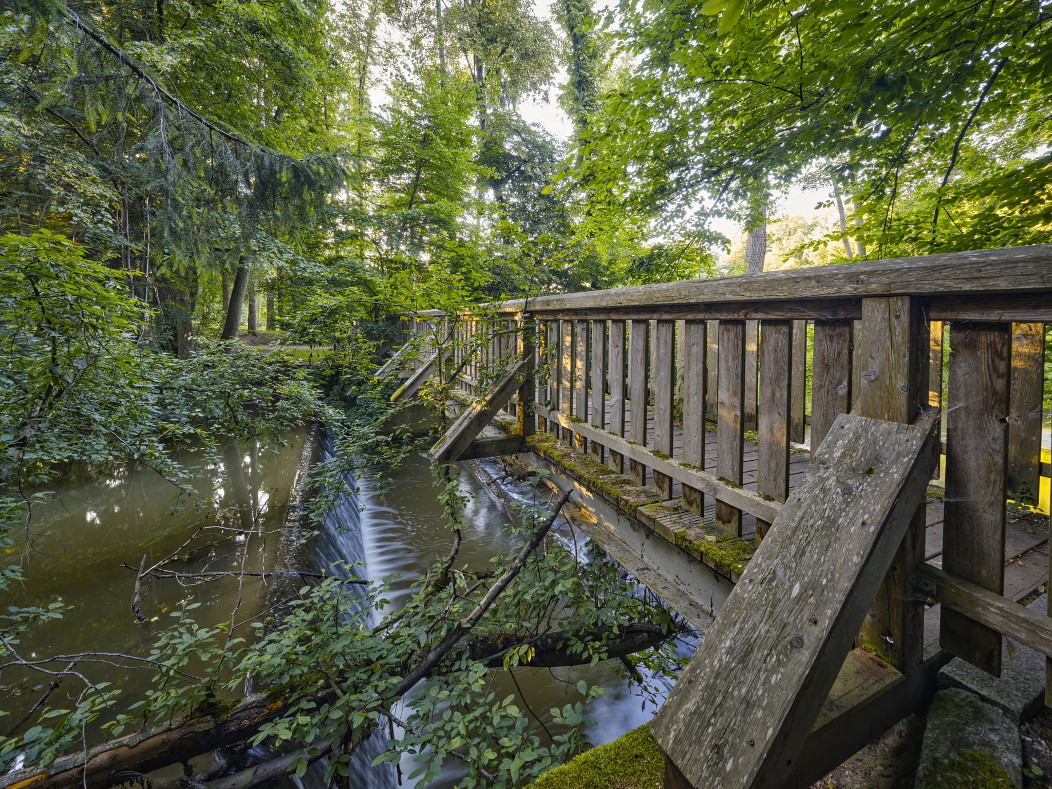 Holzbrücke im Lichtlberger Wald, Gern, Eggenfelden, Rottal-Inn, Niederbayern, Deutschland. Natürliche Waldlandschaft mit Bach und Wasserfall im letzten Licht.