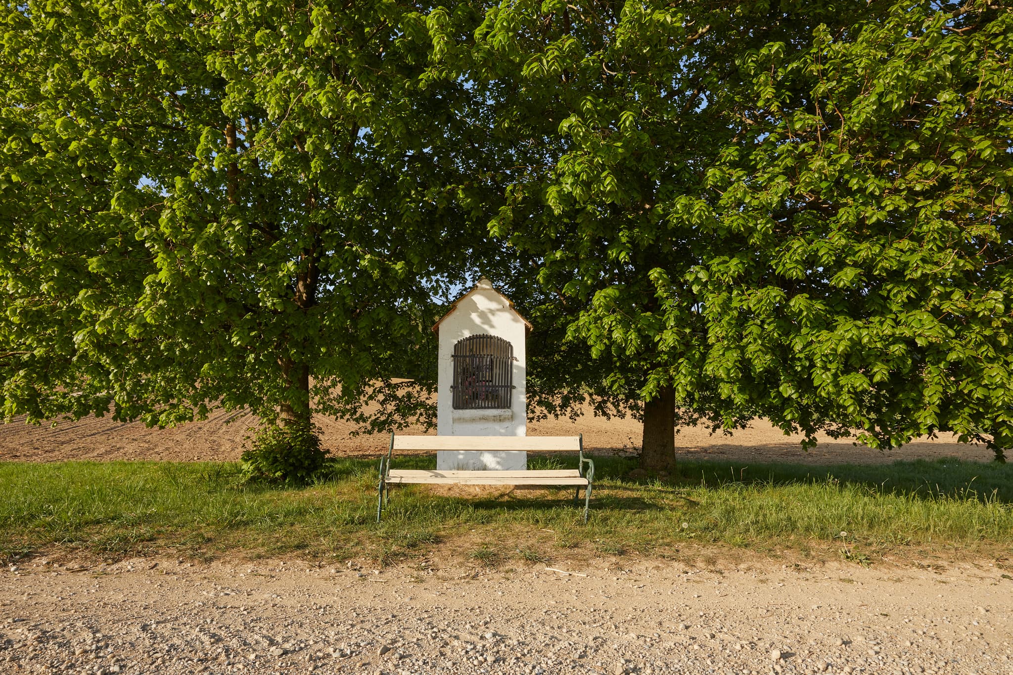 Bildstock mit Bank unter einem Baum in Erlbach, Landkreis Altötting, Oberbayern, Region Inn-Salzach, Bayern, Deutschland.