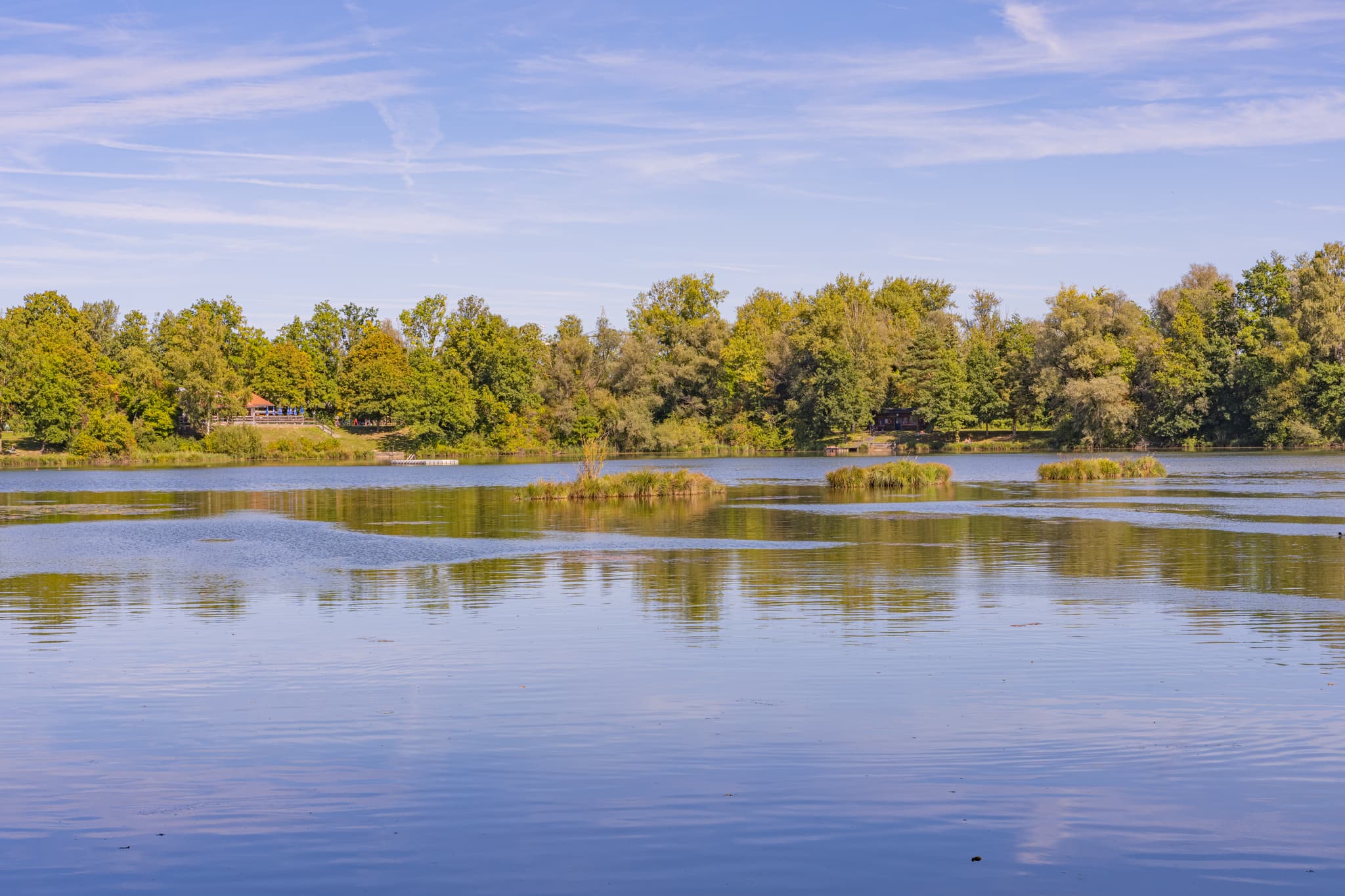 Waldsee Lago, Kirchdorf, Rottal-Inn, Niederbayern. Badesee im Bäderdreieck in Deutschland. Grüne Ufer und blauer Himmel spiegeln sich im Wasser.