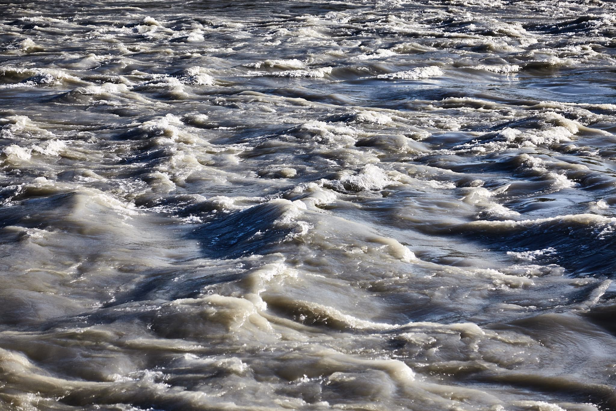 Detailansicht der Oberfläche des Inns mit wogendem Wasser in Mühldorf am Inn, Oberbayern. Diese dynamische Flusslandschaft prägt die Region Inn-Salzach.