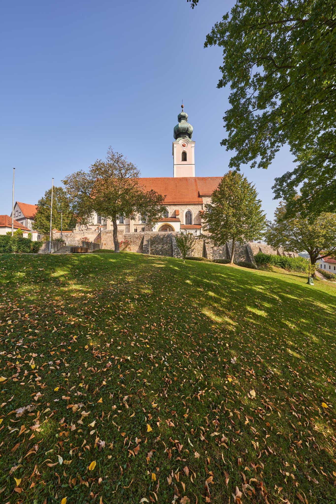 Pfarrkirche St. Michael in Mehring, Altötting, Oberbayern, Inn-Salzach, Deutschland. Herbstlaub im Vordergrund unter blauem Himmel.