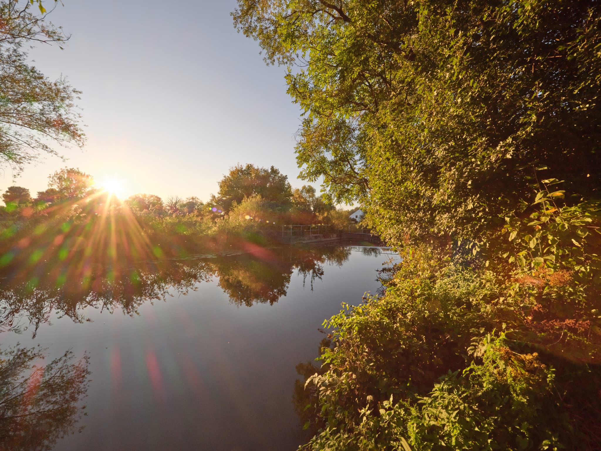 Löfflmühle Rott Wehr bei Hebertsfelden, Rottal-Inn, Niederbayern. Sonnenstrahlen beleuchten die ruhige Flusslandschaft und das bewaldete Ufer im Holzland.