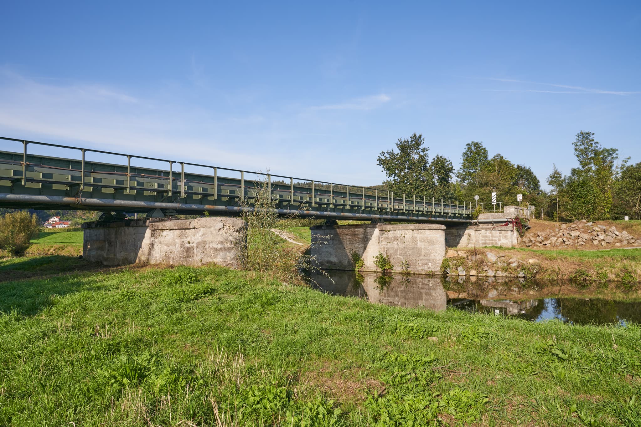 Brücke über die Isen in Kronberg, Winhöring, Landkreis Altötting, Oberbayern. Grüne Uferlandschaft in der Inn-Salzach Region, Deutschland, unter klarem Himmel.