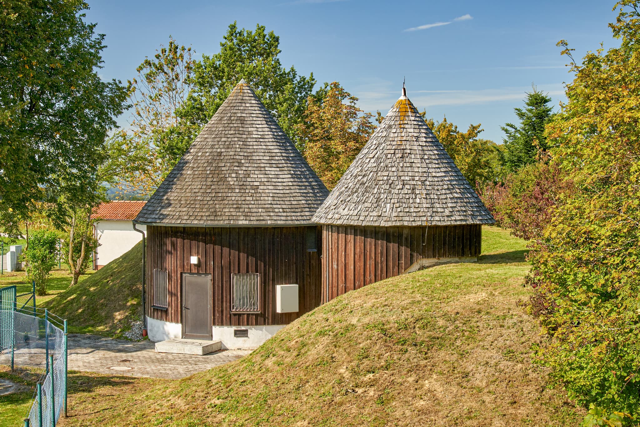 Zwei Holzhäuschen mit Spitzdächern auf Funkturmgelände Schnaitsee, Traunstein, Oberbayern, Chiemgau, Deutschland. Ungewöhnliche Gebäude in grüner Landschaft.