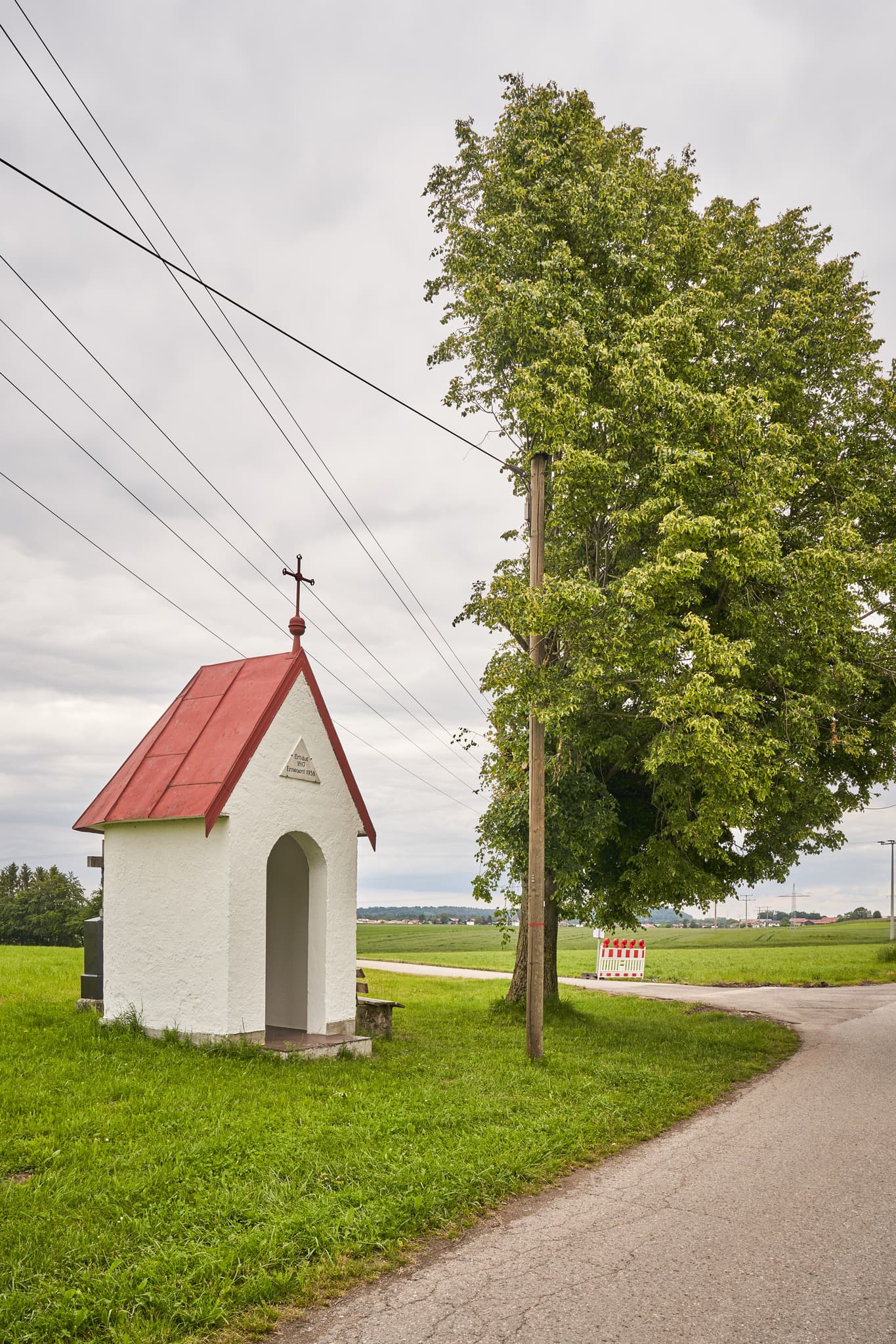 Ein Bildstock mit Grabstein in Höresham, Burgkirchen, Altötting, Oberbayern, Inn-Salzach, Deutschland. Diese Gedenkstätte zeigt Felder und einen halben Baum.