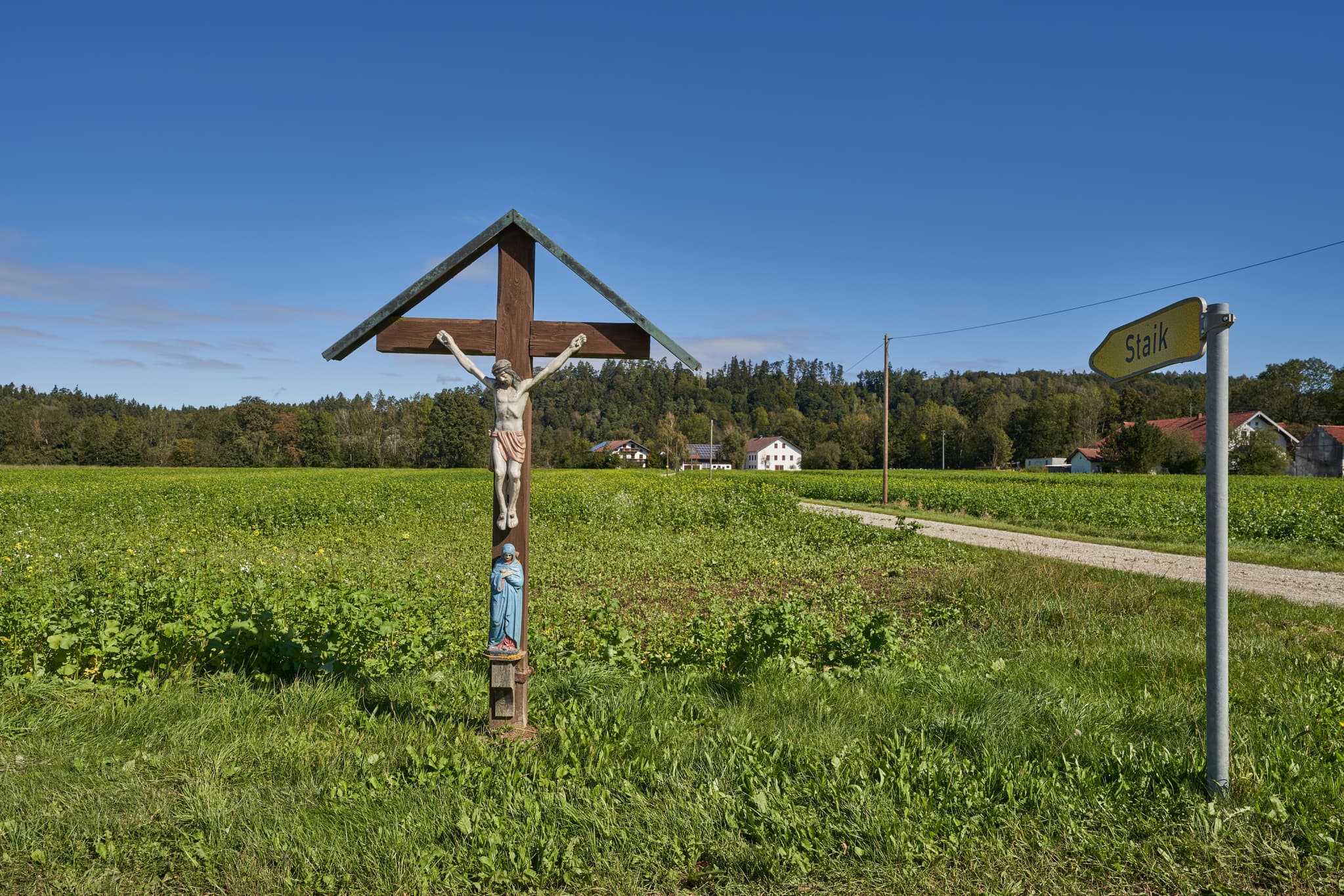 Wegkreuz auf einem Feldweg in Staik, Winhöring, Landkreis Altötting. Die ländliche Landschaft im Inn-Salzach-Gebiet Oberbayerns, Deutschland, mit Feldern.