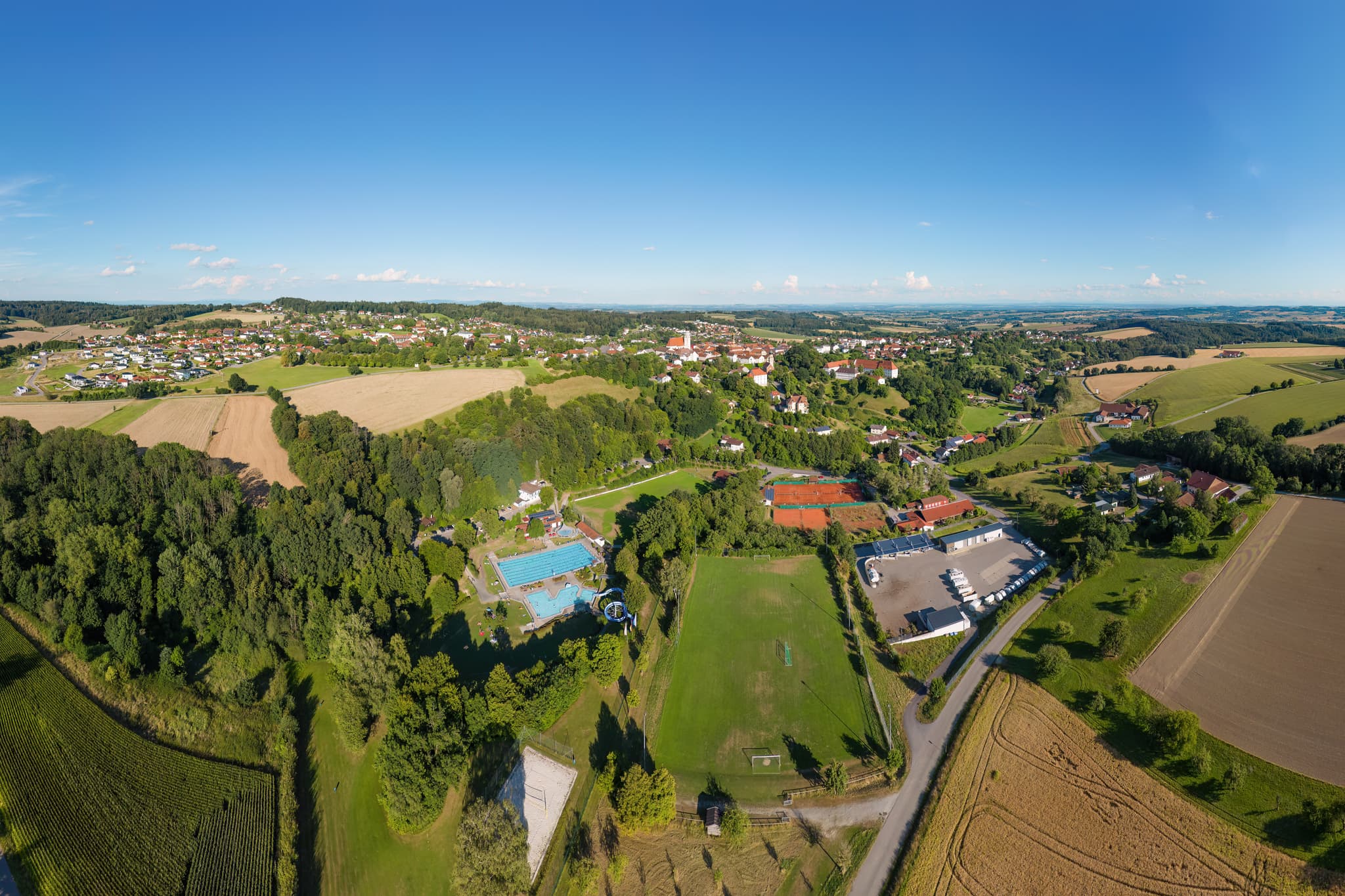 Ein weitläufiges Luftbild von Bad Griesbach im Rottal, Landkreis Passau, Niederbayern, Deutschland. Es zeigt das Freibad, einen Sportplatz und den Wertstoffhof.