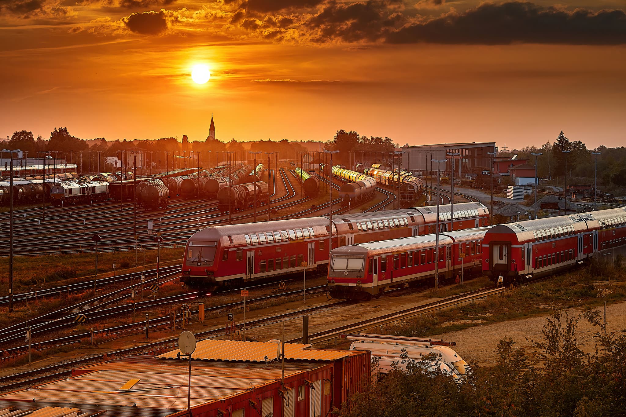 Sonnenuntergang am Bahnhof Mühldorf am Inn, Oberbayern. Züge auf den Gleisen des Bahnhofs. Die Szenerie der Region Inn-Salzach fängt die Abendstimmung ein.