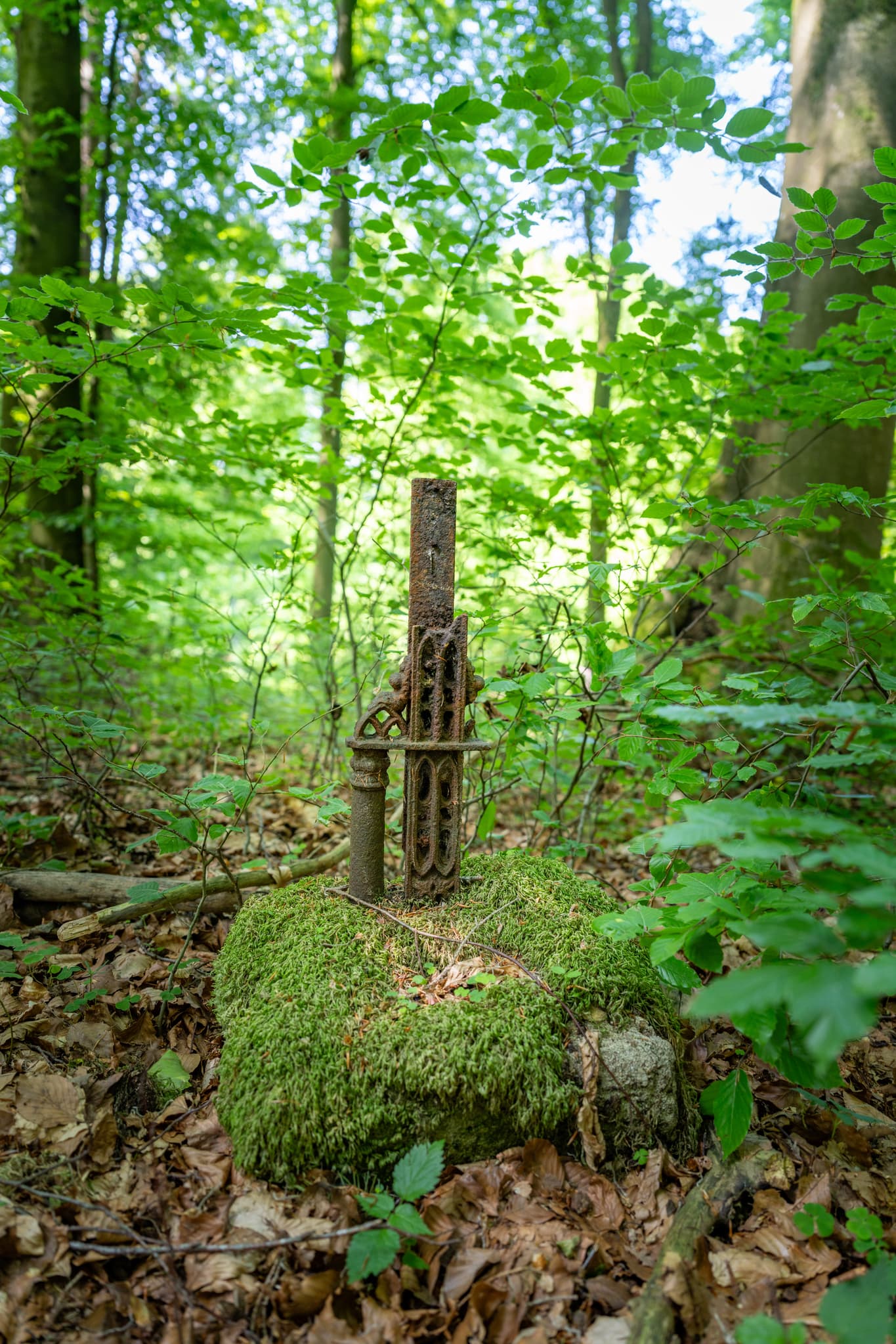 Ein rostiges Metallkreuz auf einem mit Moos bewachsenen Stein in einem Wald bei Kager, Gemeinde Reischach, Bezirk Oberbayern, Region Inn-Salzach, Deutschland.